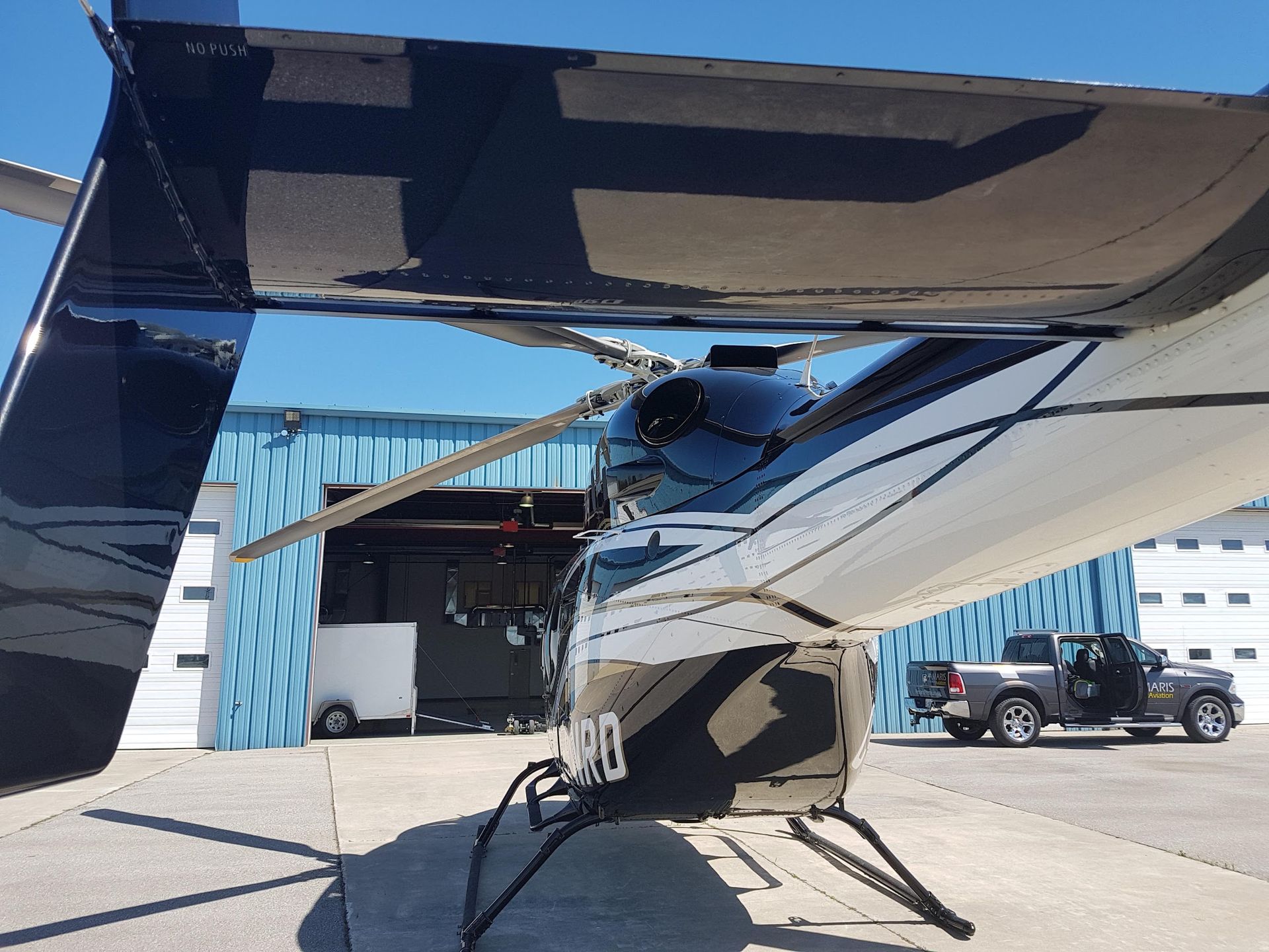 Helicopter tail and rotor blades, parked in front of a blue hangar with a truck nearby.