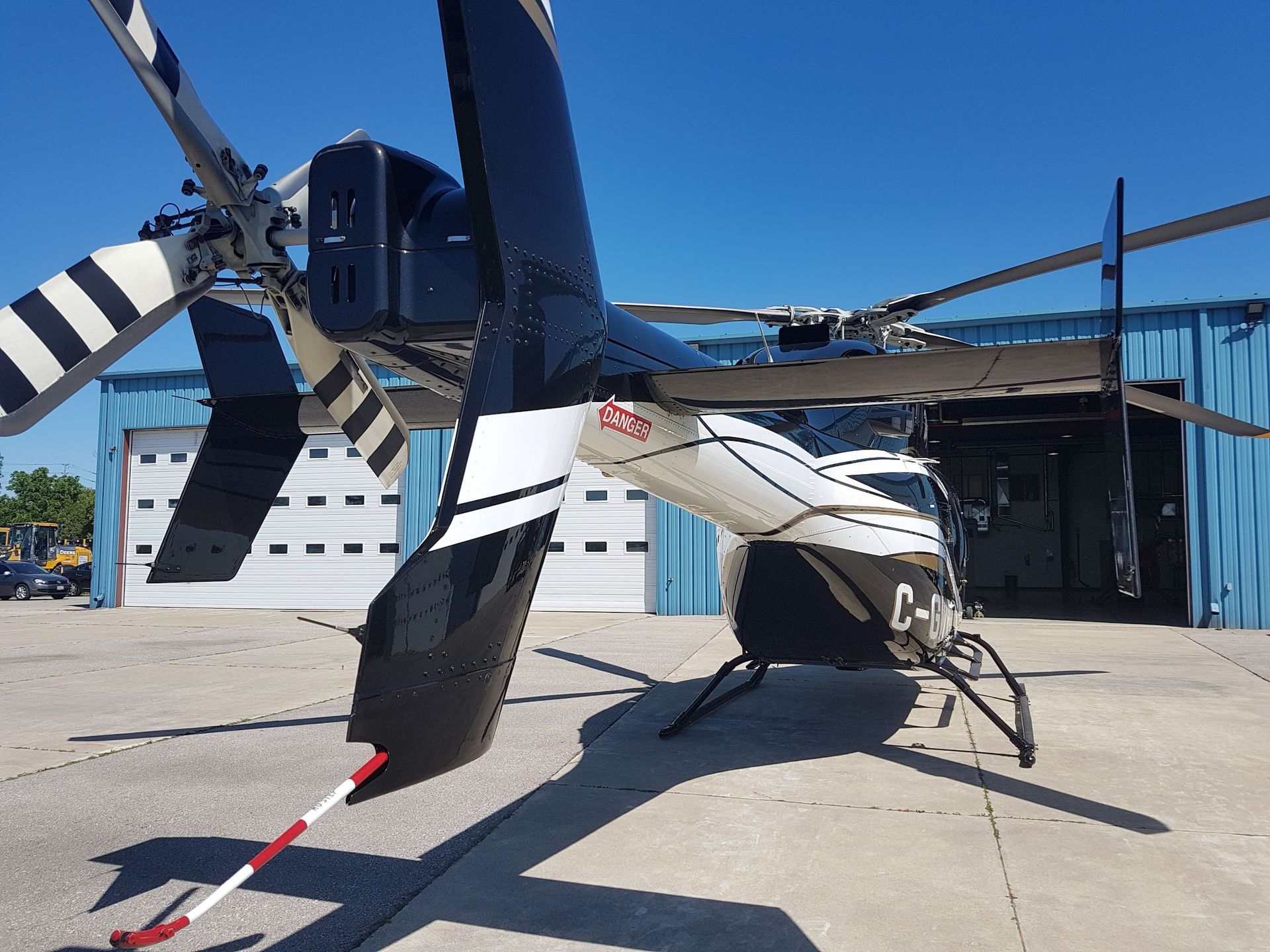 Helicopter, black and white, parked on concrete. Tail rotor and main rotor visible. Blue building in background.