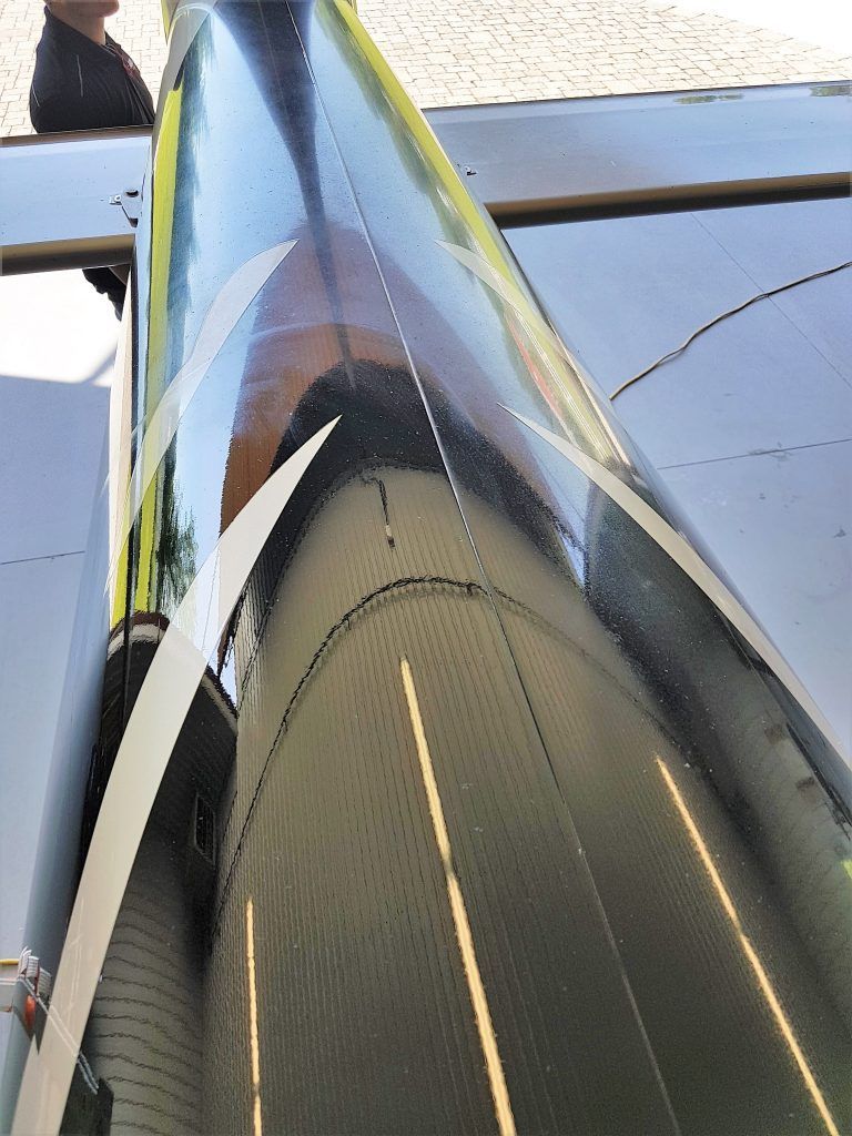 Black airplane fuselage with white stripes, reflecting light. A person stands nearby.