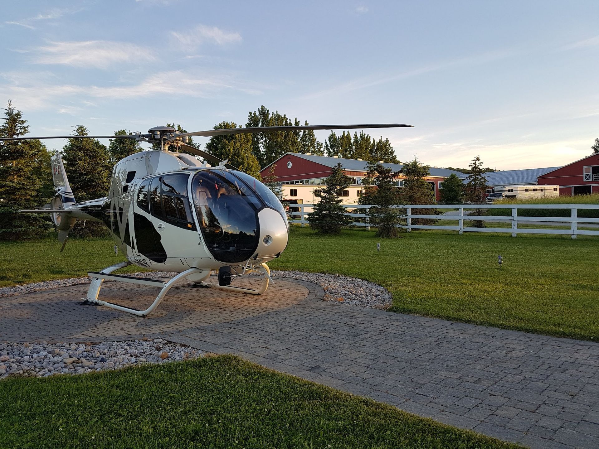 Helicopter on a circular stone pad on a grassy lawn. Red buildings and trees are in the background.