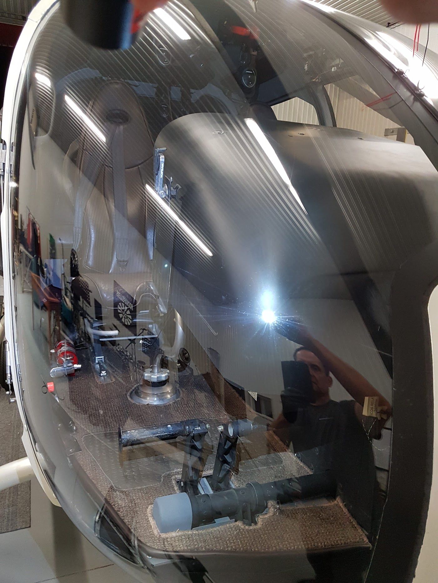 Helicopter cockpit interior with reflections of a person, equipment, and bright light.