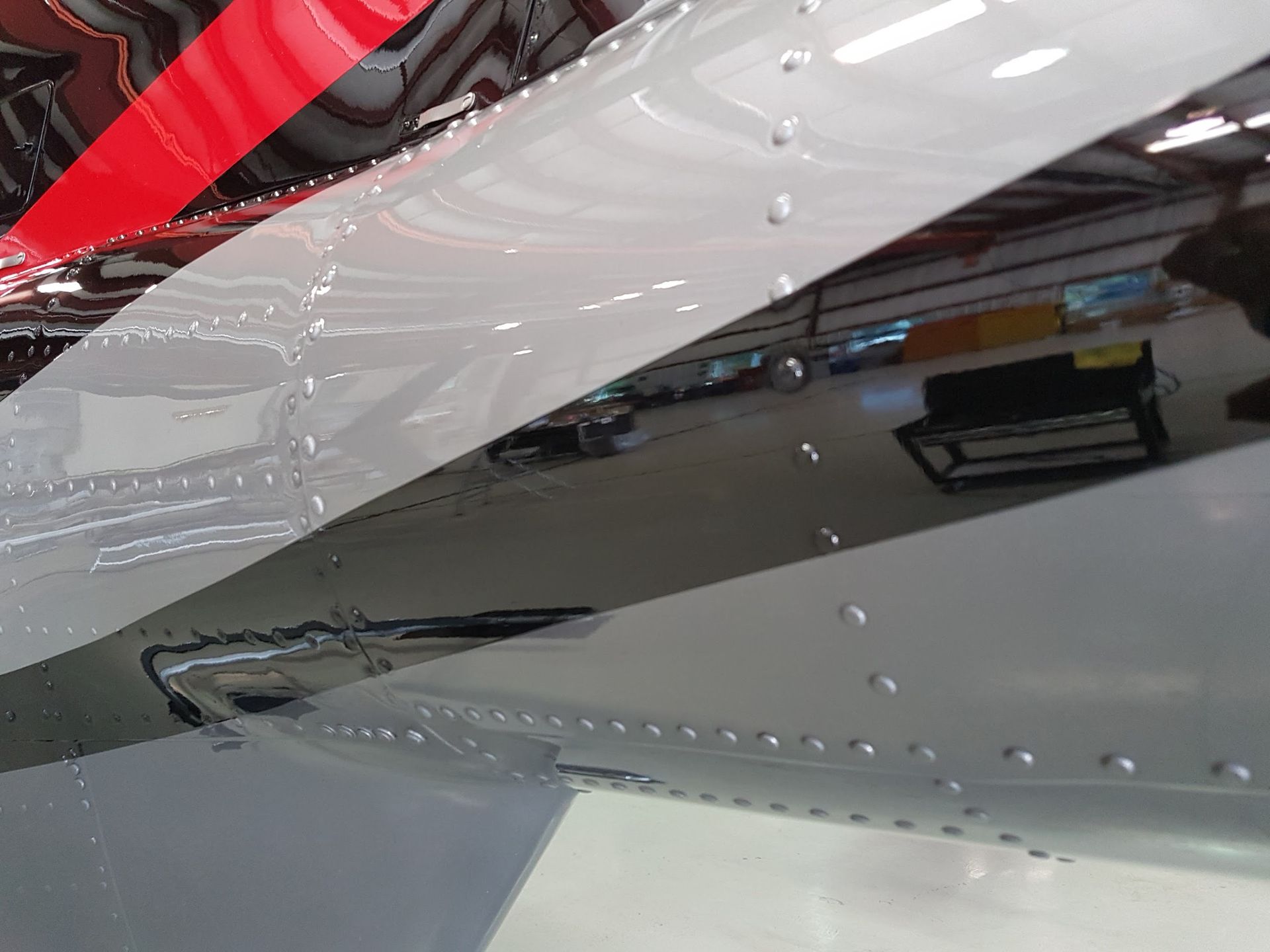 Close-up of airplane wing with silver, black, and red paint, rivets visible.