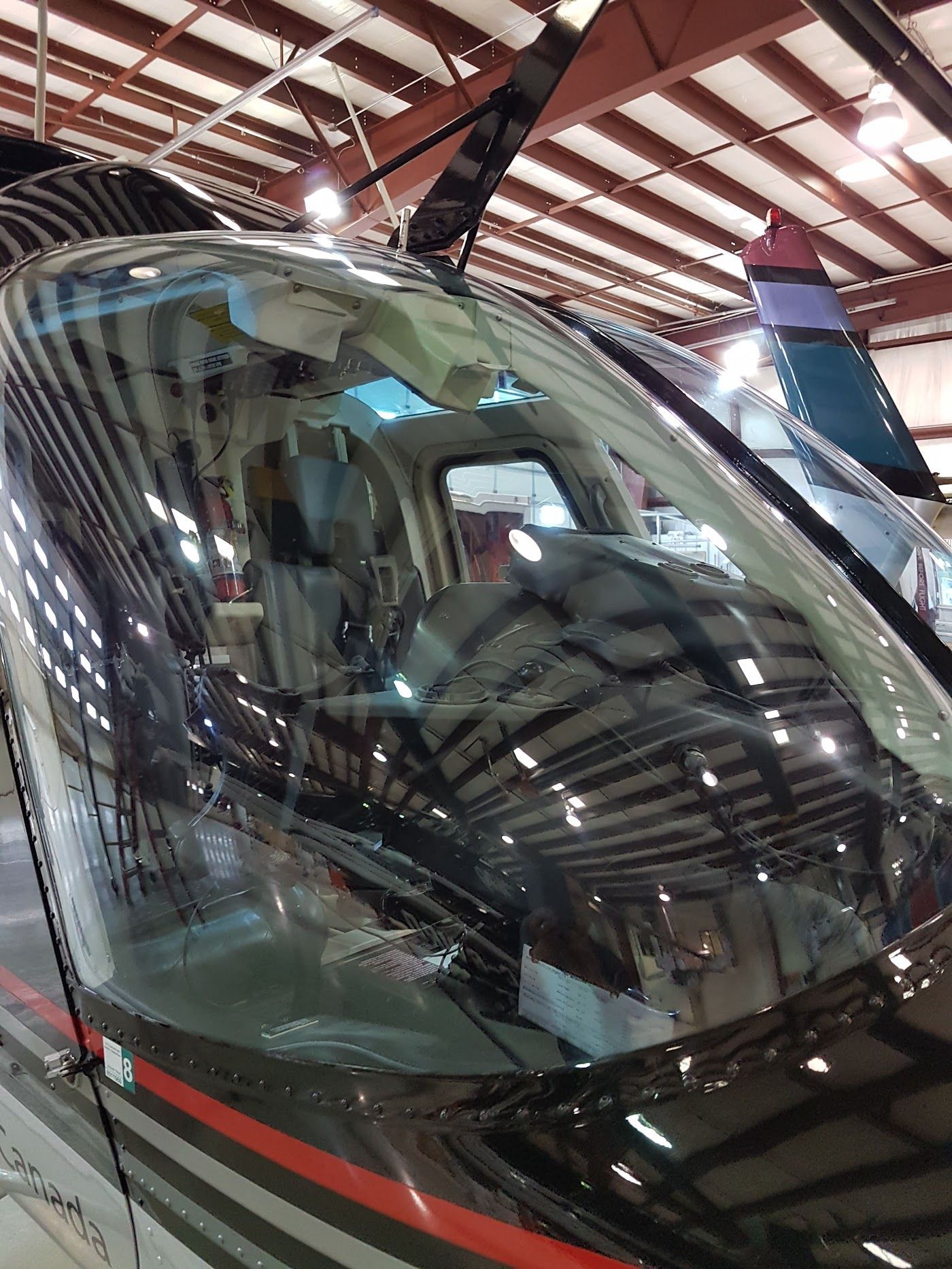 Helicopter cockpit view, reflections in windshield. Black and red details. Hangar setting.