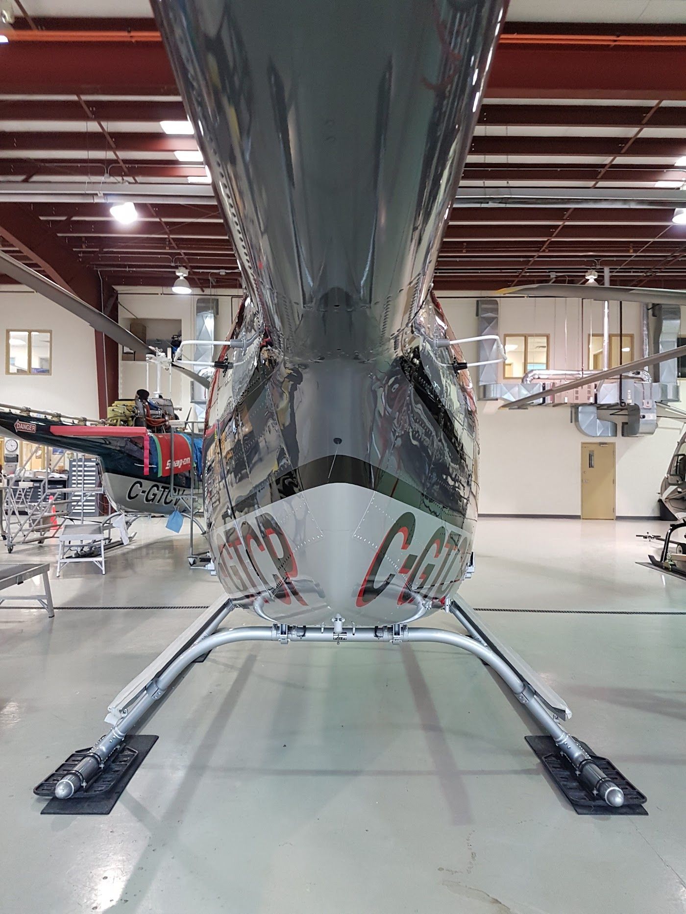 Helicopter inside hangar, head-on view. Silver and dark grey body, landing skids,