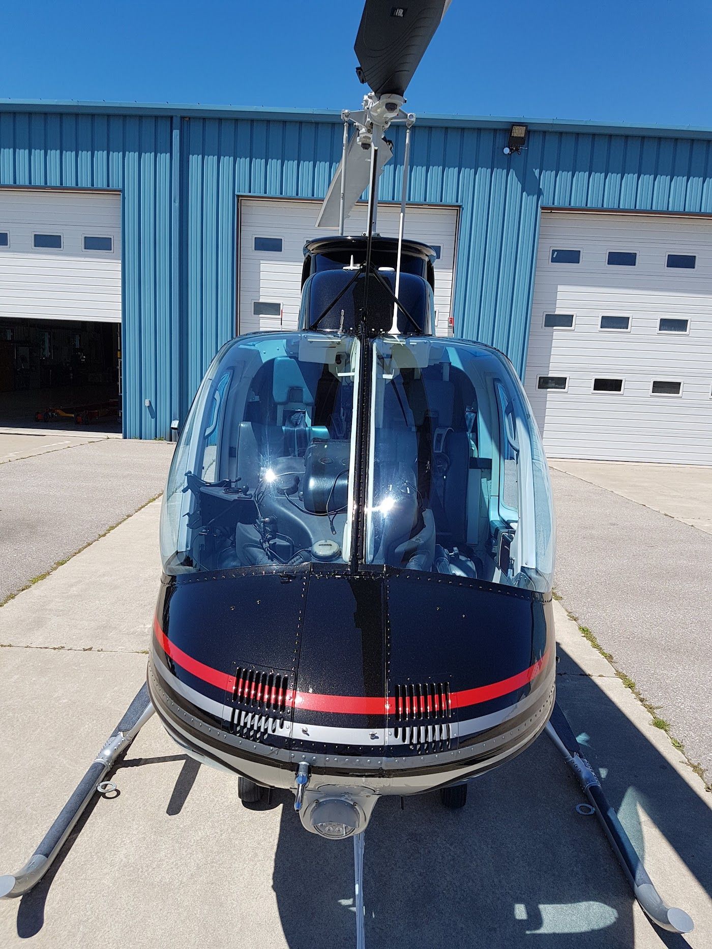 Black helicopter with red stripes in front of a blue hangar.