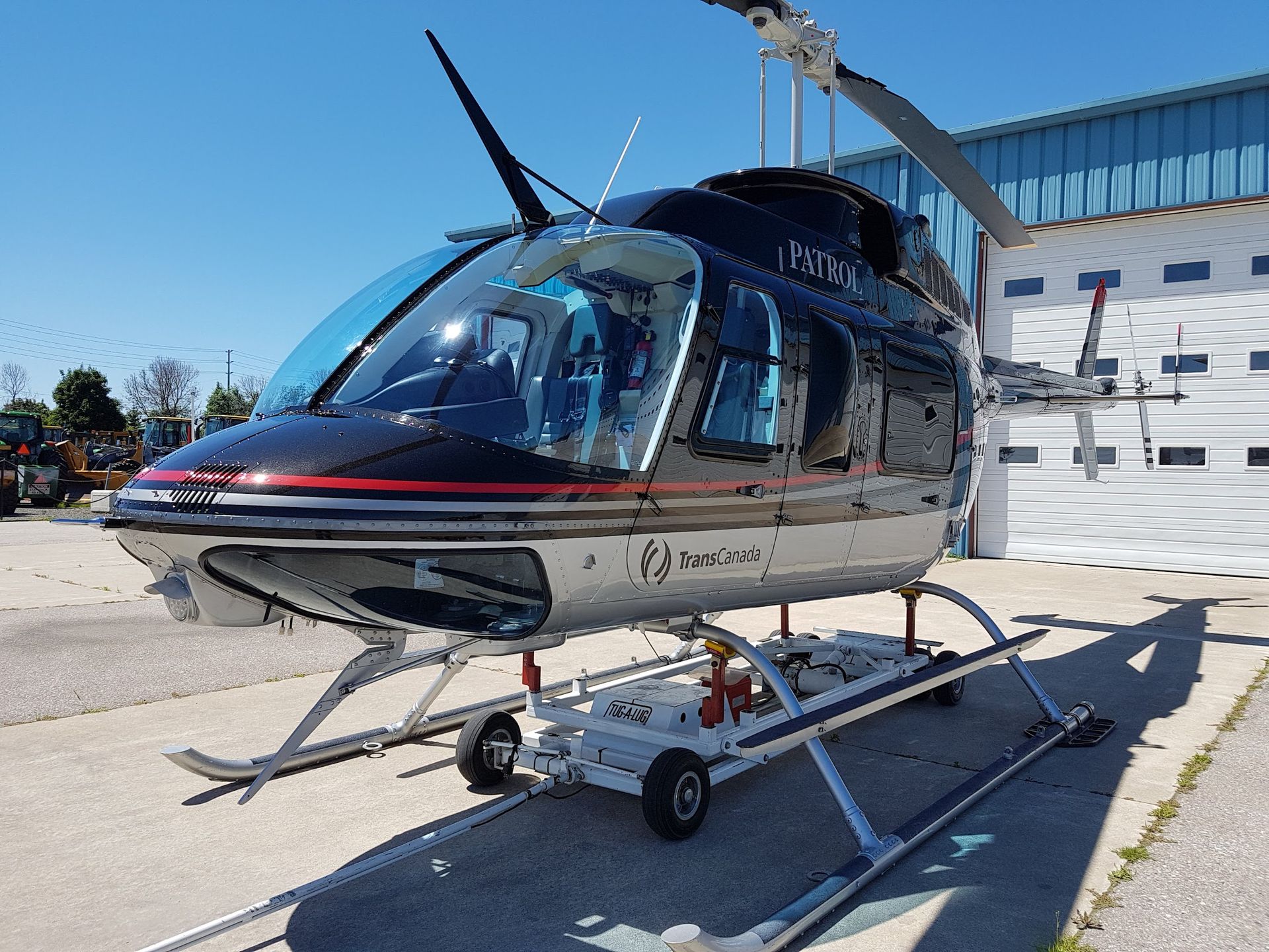 Black and silver helicopter on a dolly outside, under a blue sky, near a building with a white garage door.