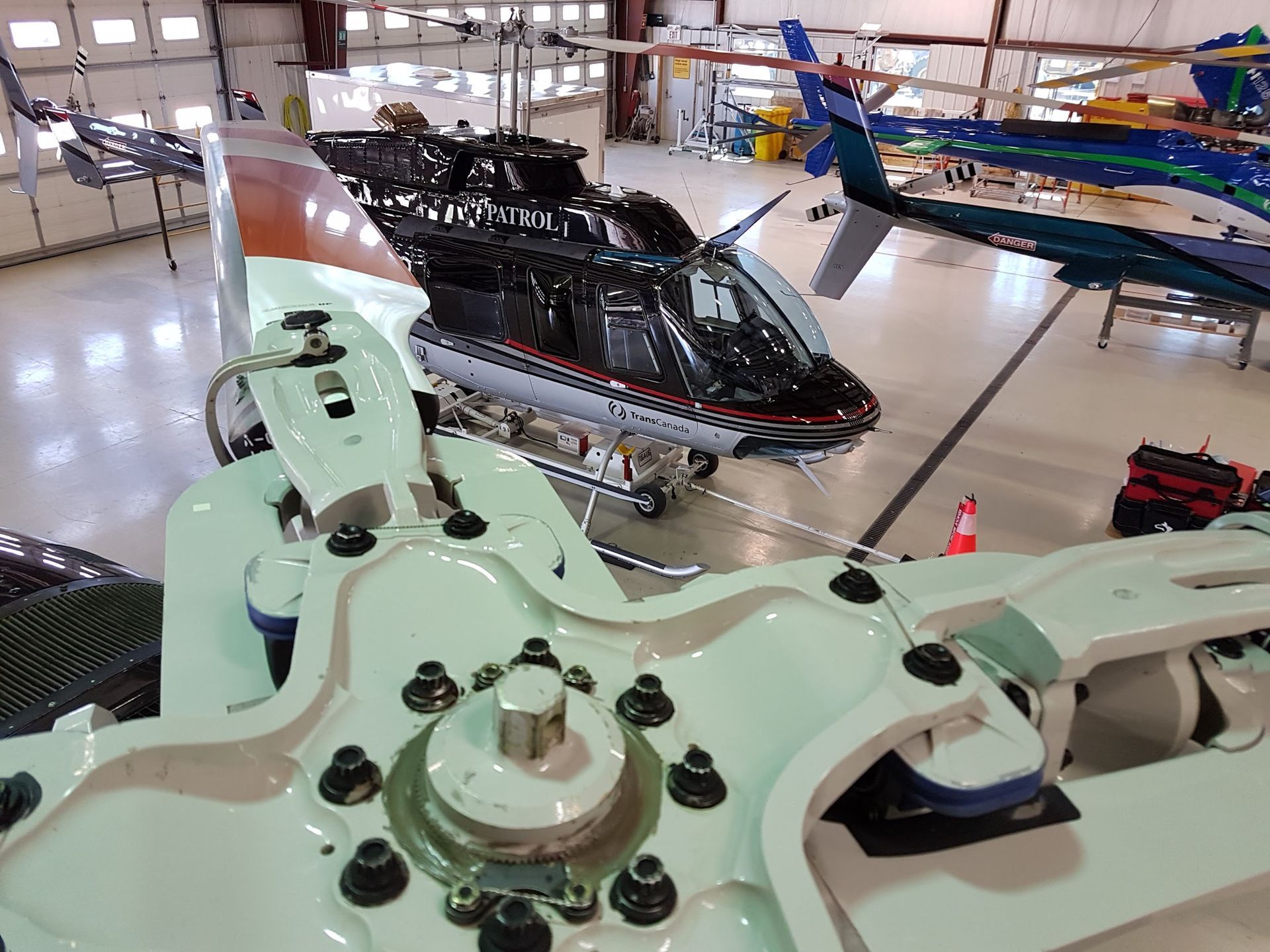 Helicopters inside a hangar; focus on rotor blades. Various aircraft are parked inside.