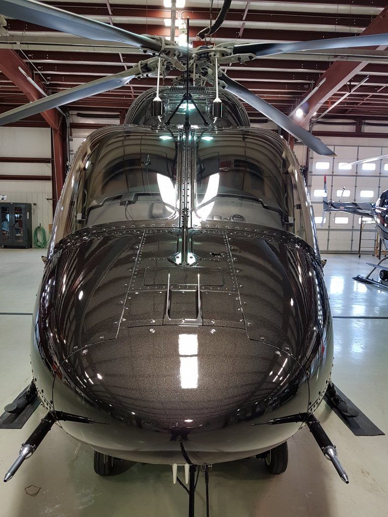 Black helicopter in hangar, front view. Reflective surface, rotors, landing gear visible.