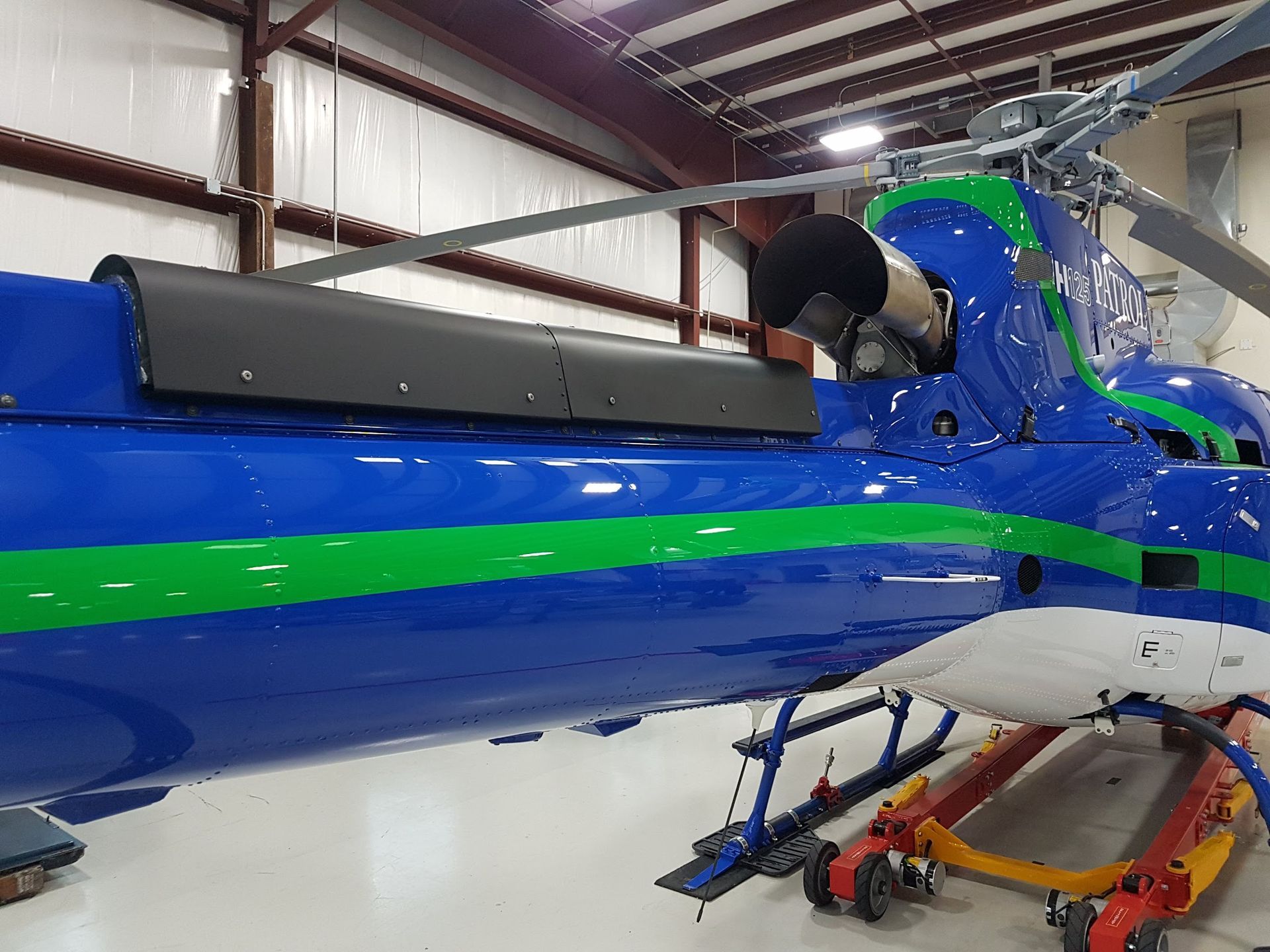 Blue and green helicopter in a hangar with black panels on its side and red and white support wheels.