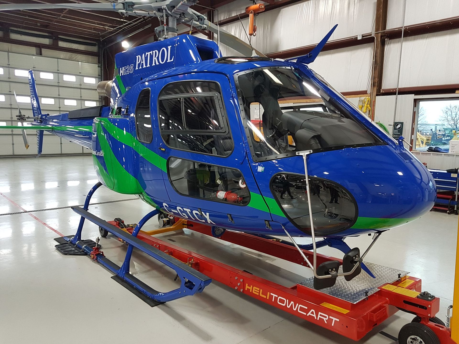 Blue and green helicopter on a red cart inside a hangar, labeled