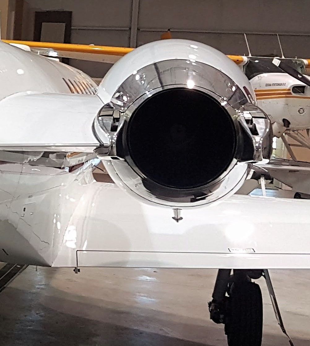 Jet engine exhaust nozzle on a white aircraft wing, gleaming chrome, inside a hangar.