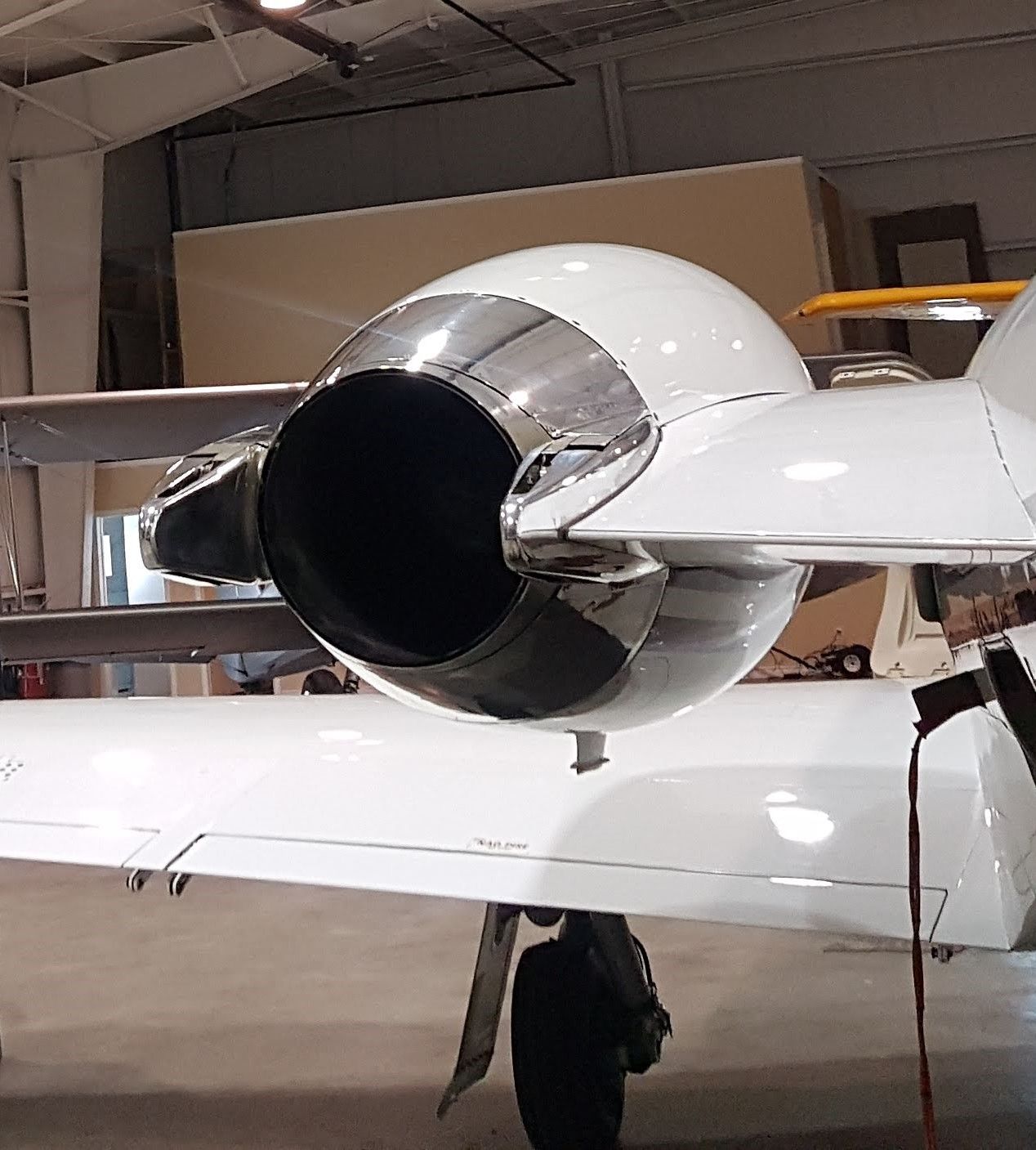 Close-up of a jet engine on a white aircraft wing, showing the engine's polished metal and a black exhaust.