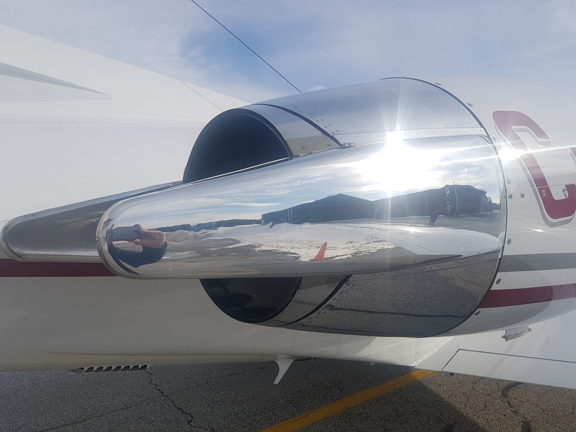 Shiny jet engine on a white aircraft, reflecting sky and landscape.