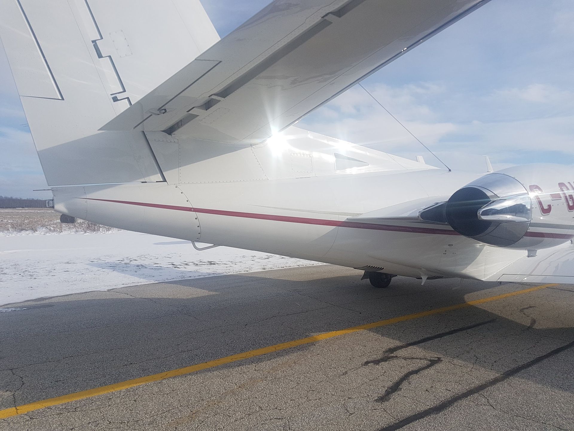 White airplane on a tarmac with red stripe. Snow and blue sky in the background.