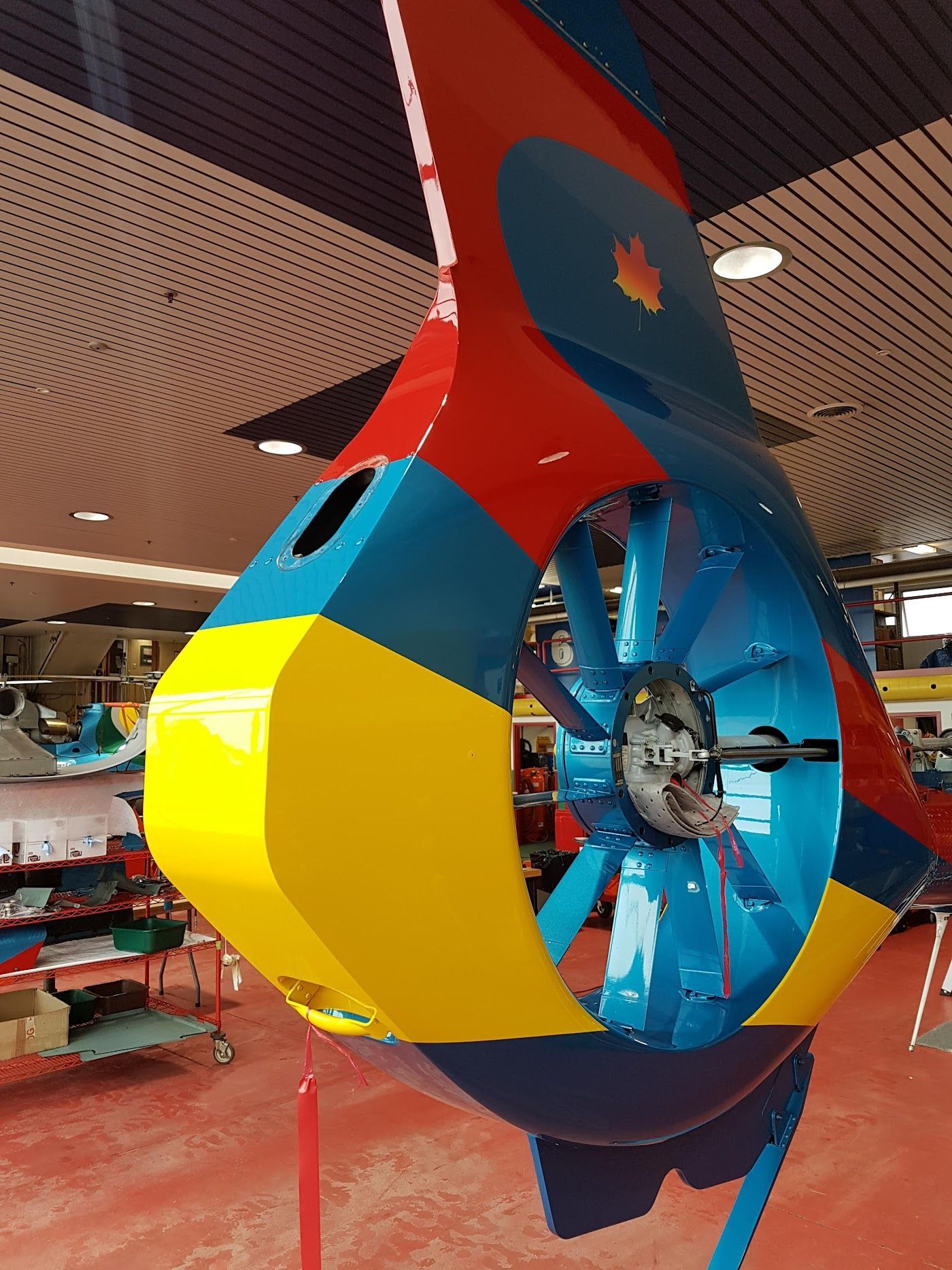 Colorful helicopter tail with blue, yellow, and red sections; rotor visible. Indoor setting.