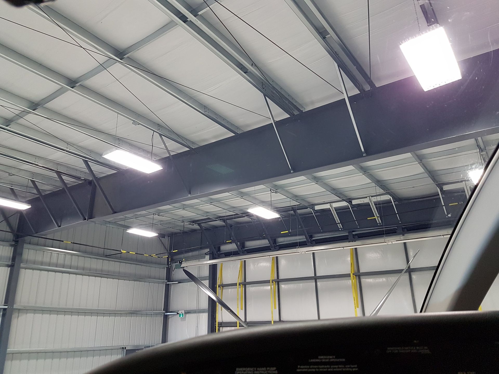 Interior of an aircraft hangar with overhead ductwork and lights. View from inside a cockpit looking up.