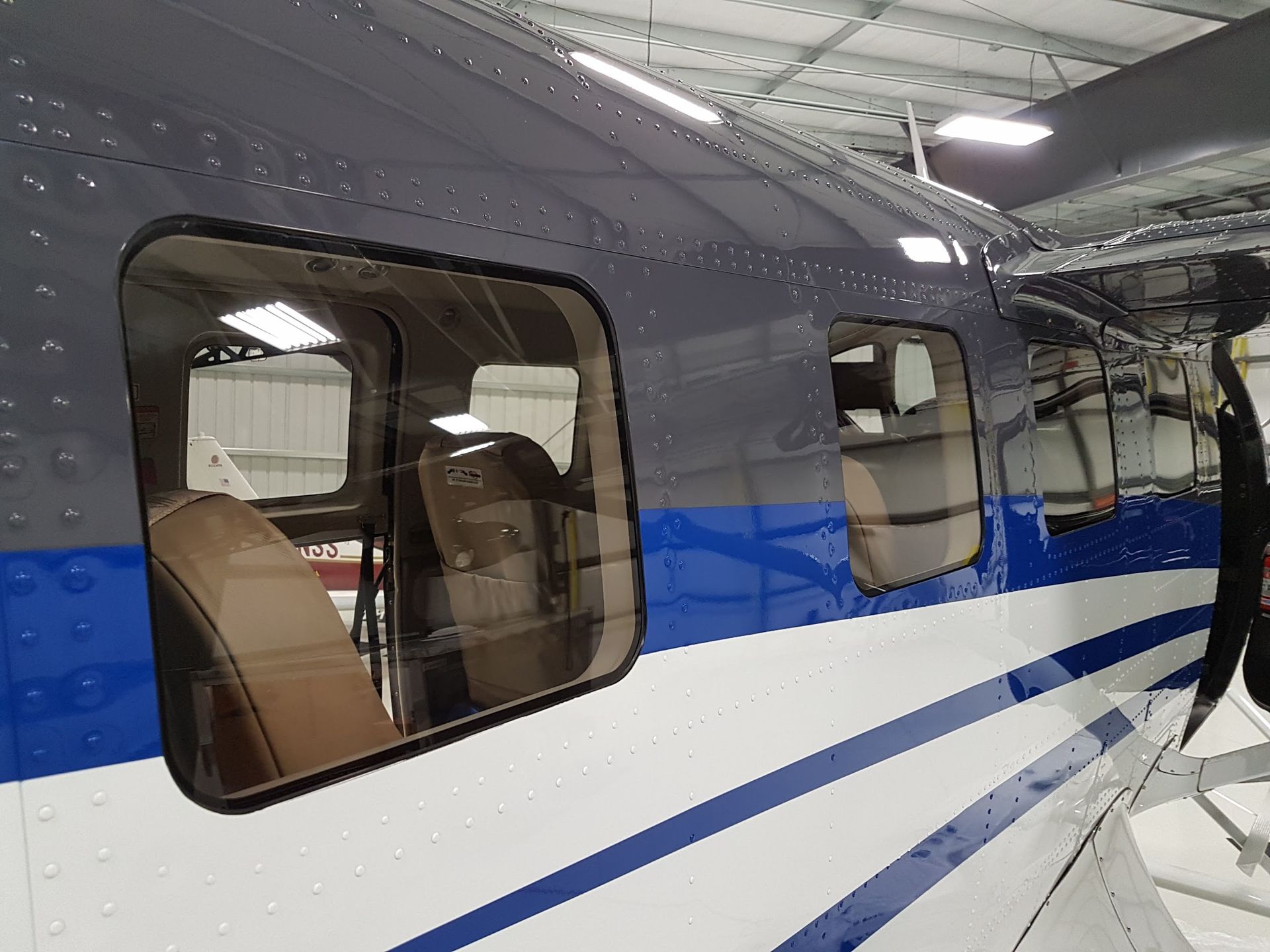Side view of a blue, white, and gray airplane with windows, a propeller, and an interior seat visible.