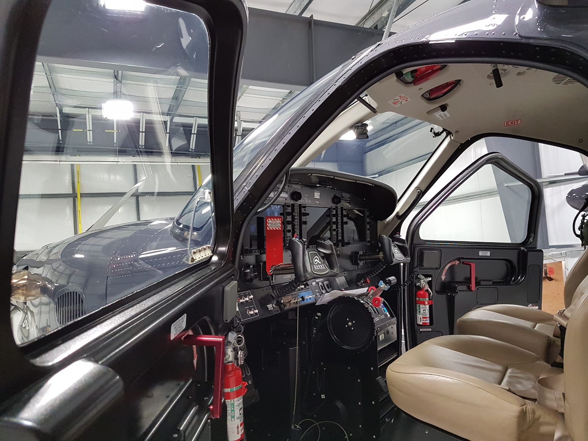 Inside the cockpit of a gray aircraft, showing seats, controls, and open side door.