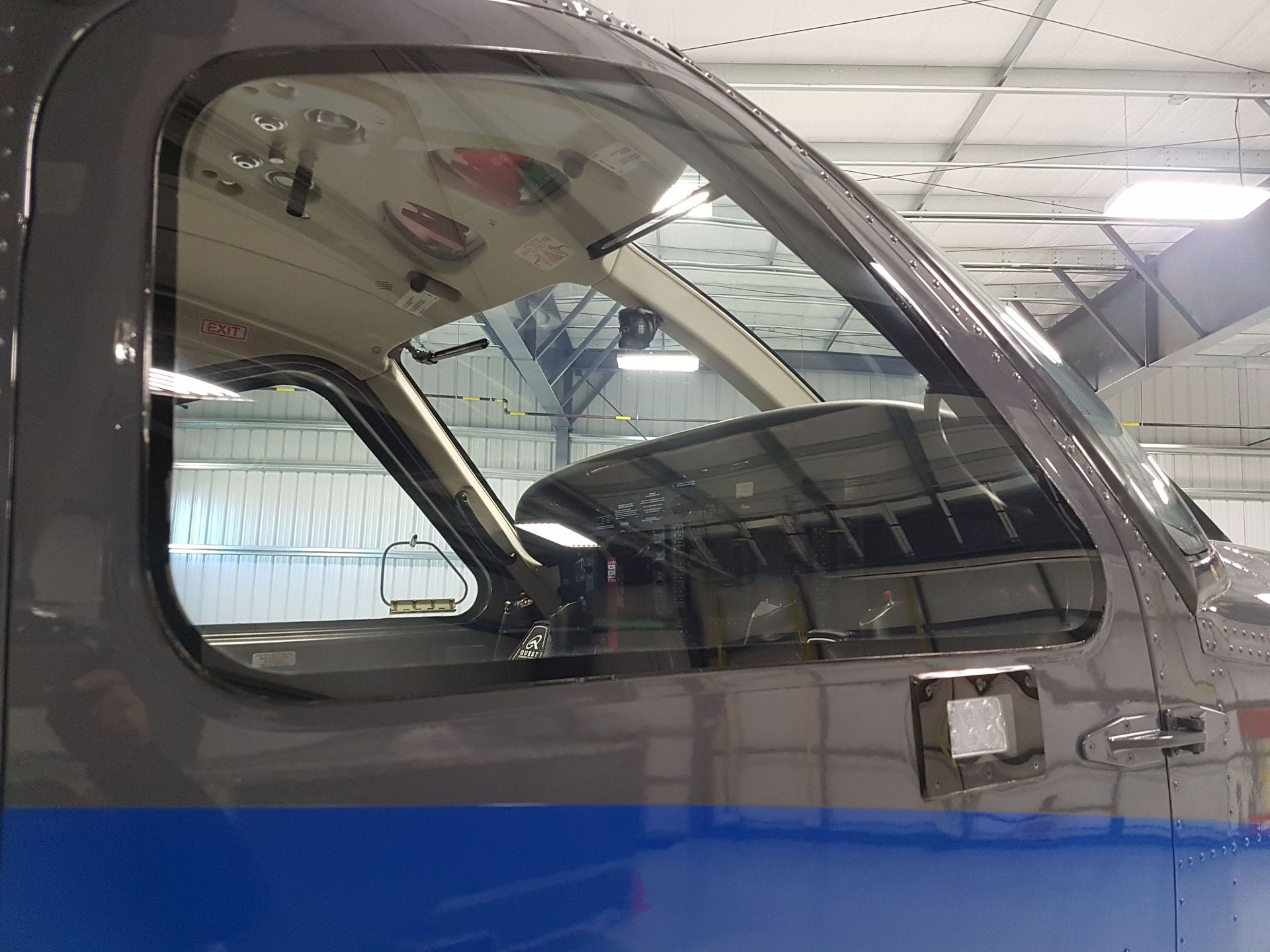 Airplane cockpit window with gray and blue exterior, view of interior and hangar.