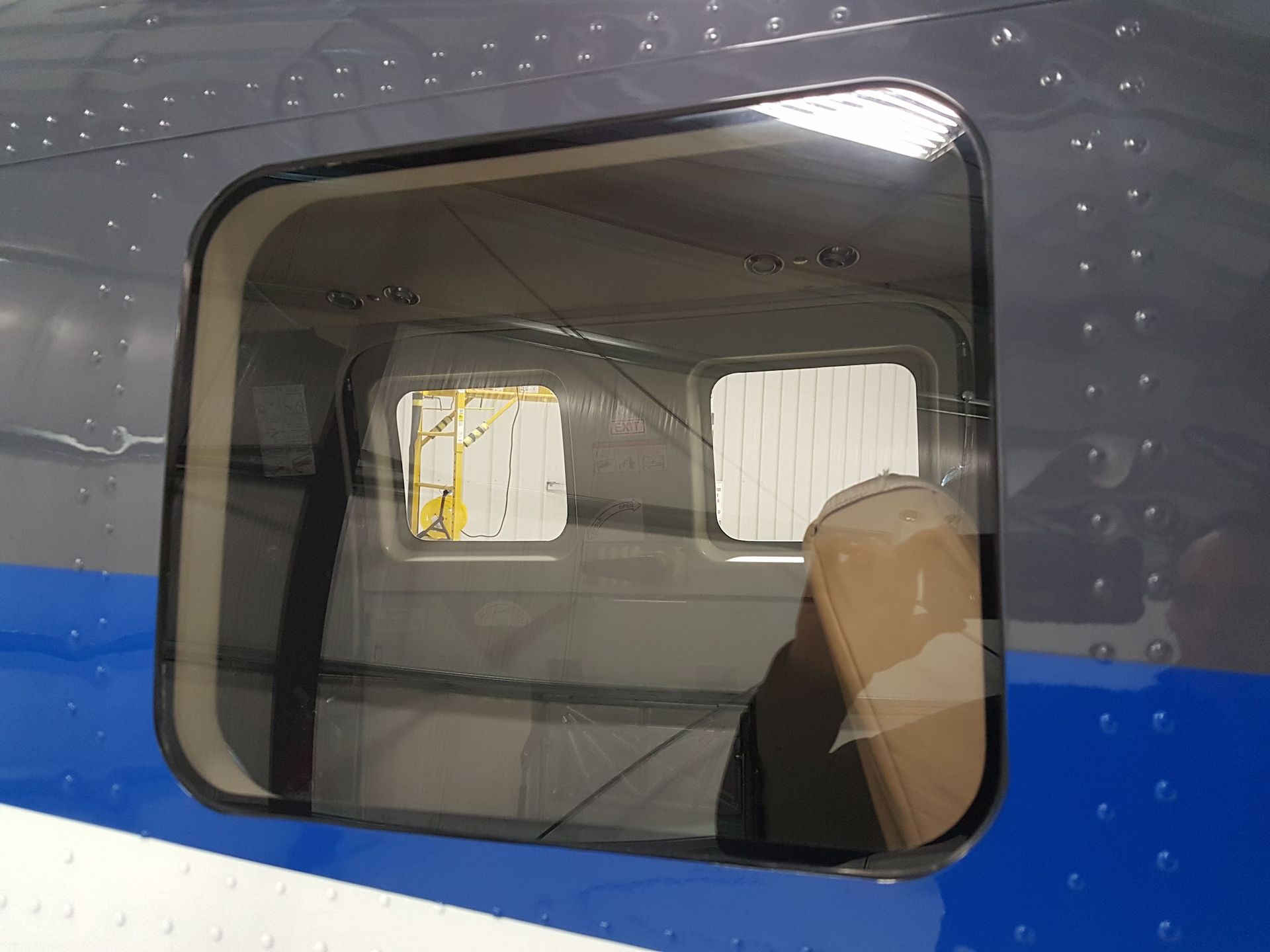 Airplane window showing interior, with the outside environment visible through two smaller windows.