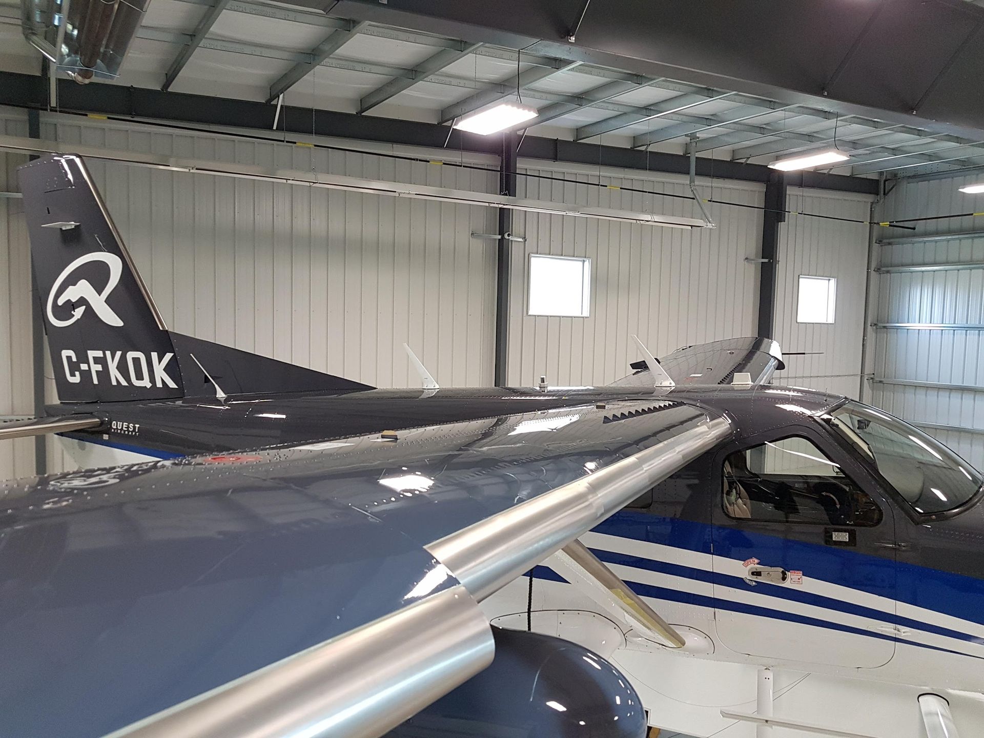 Dark blue airplane inside a hangar, tail with C-FKQK registration.