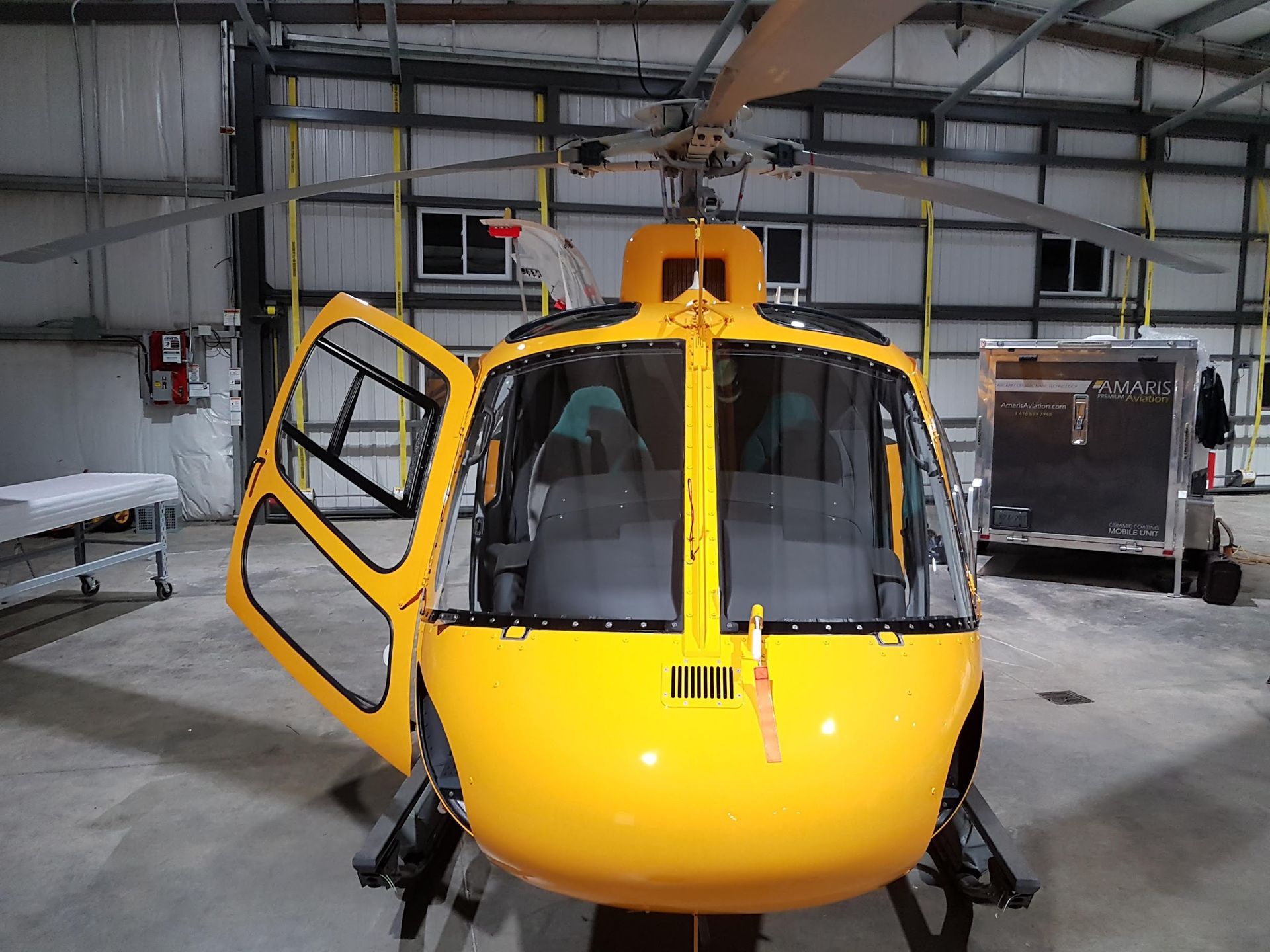 Yellow helicopter with open door inside a hangar.