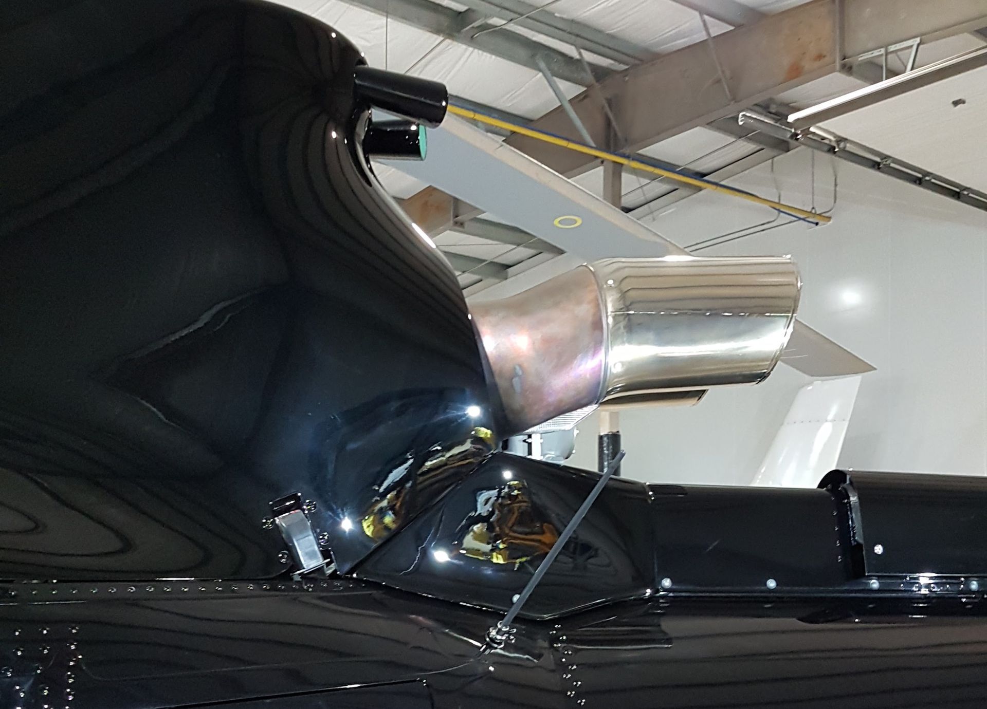 Black jet aircraft tail with silver engine exhaust, inside a hangar.