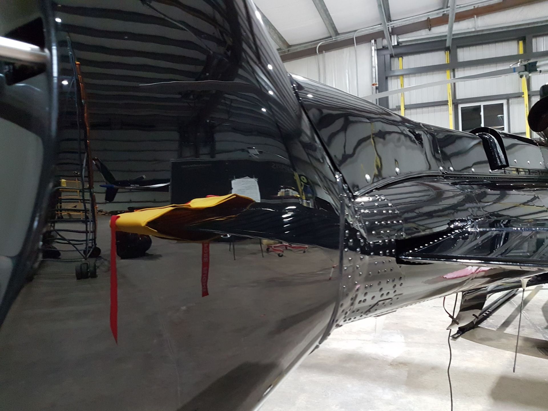 Shiny black aircraft tail in a hangar, reflecting the interior and surrounding equipment.