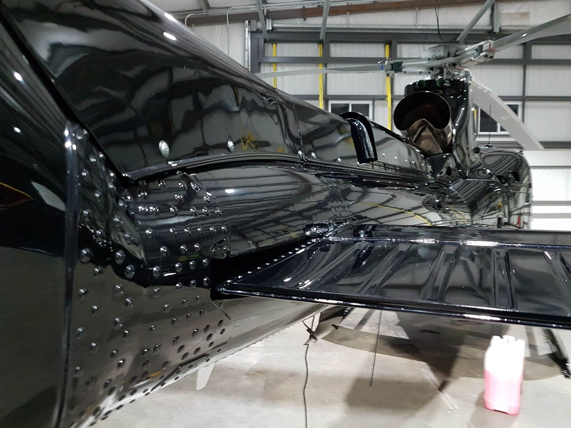 Black helicopter tail with rivets, in a hangar.