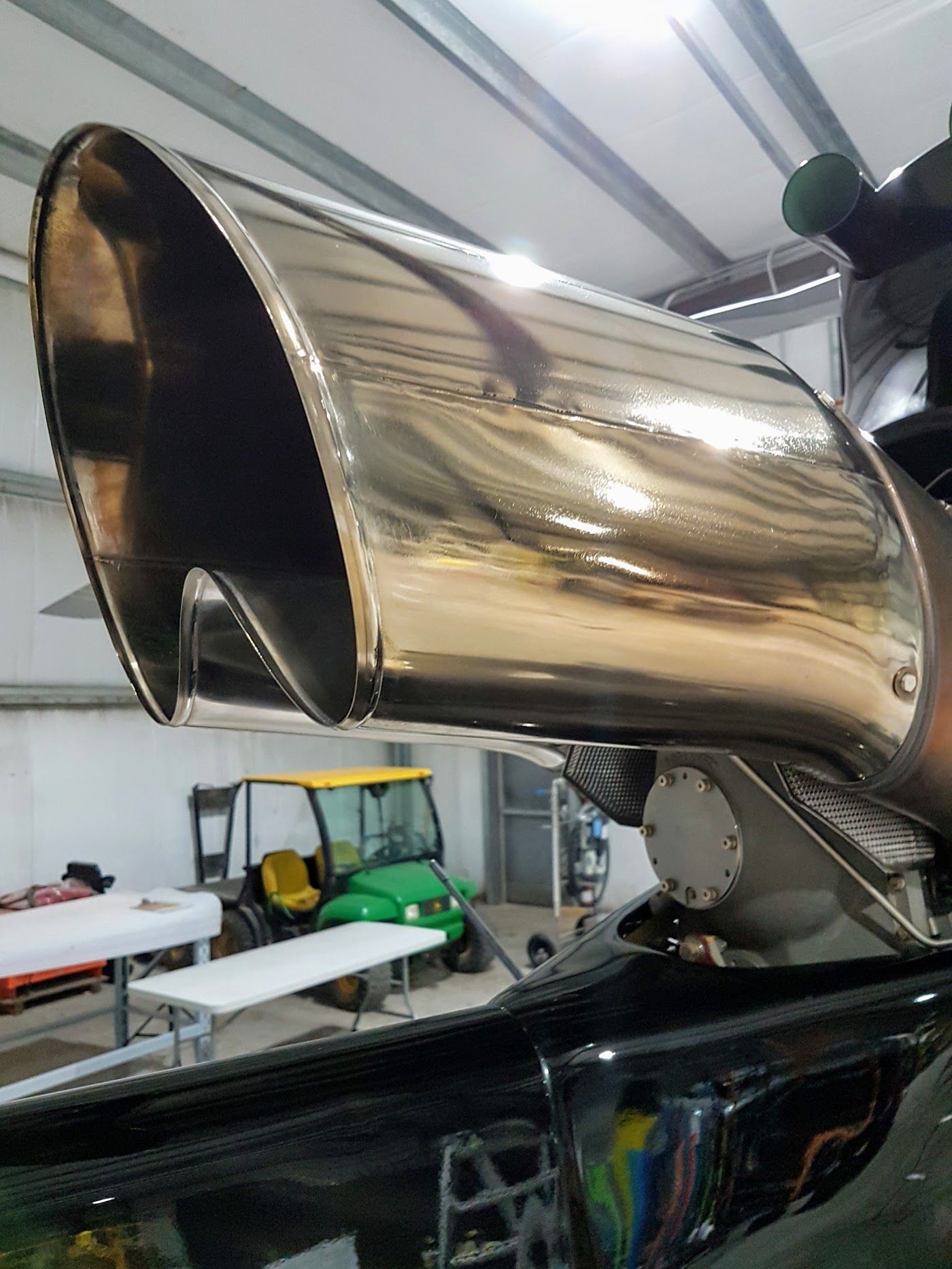 Shiny chrome exhaust pipe, possibly from a vehicle, with a golf cart visible in the background.