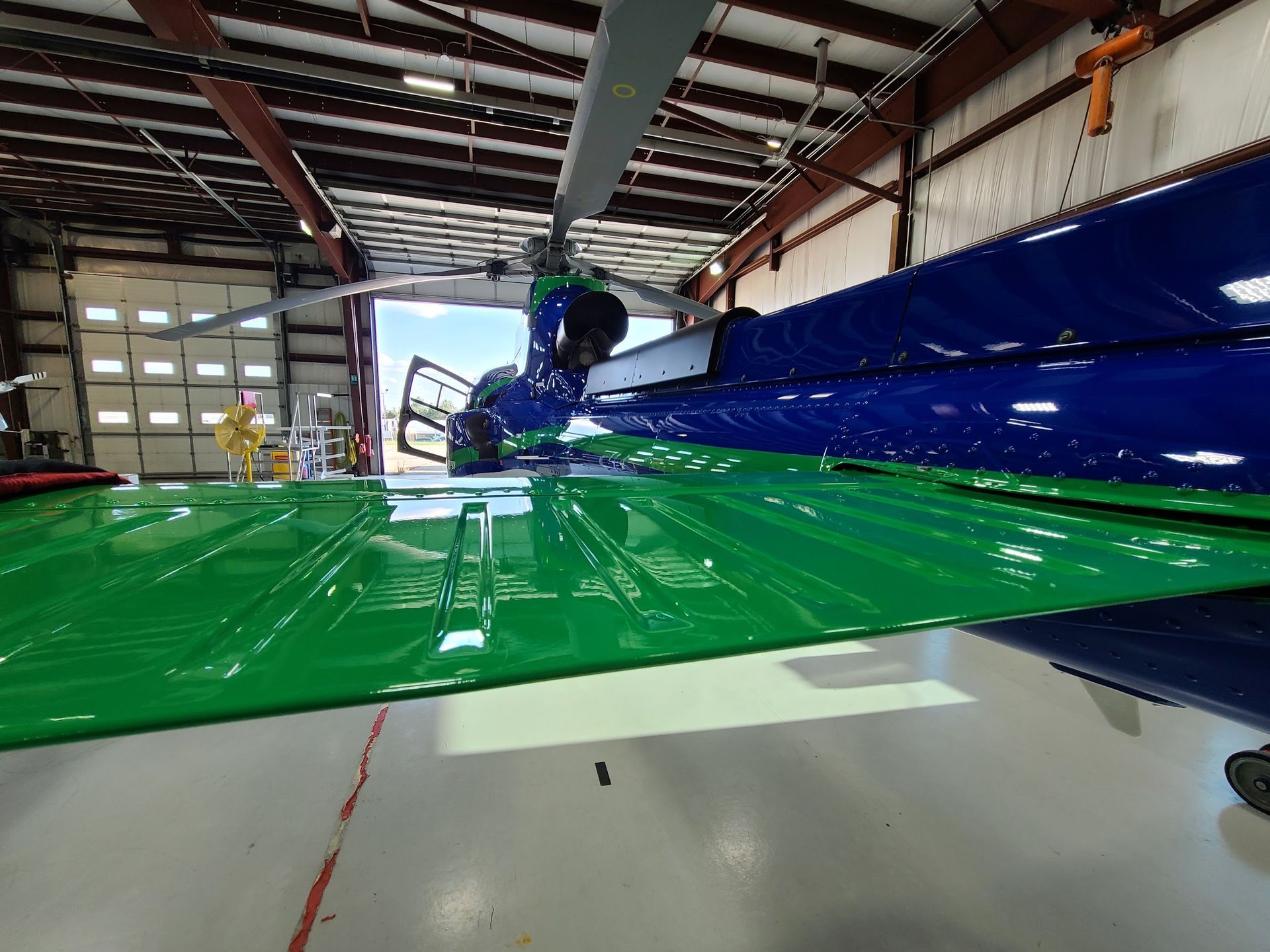 Green and blue helicopter inside a hangar with the door open.