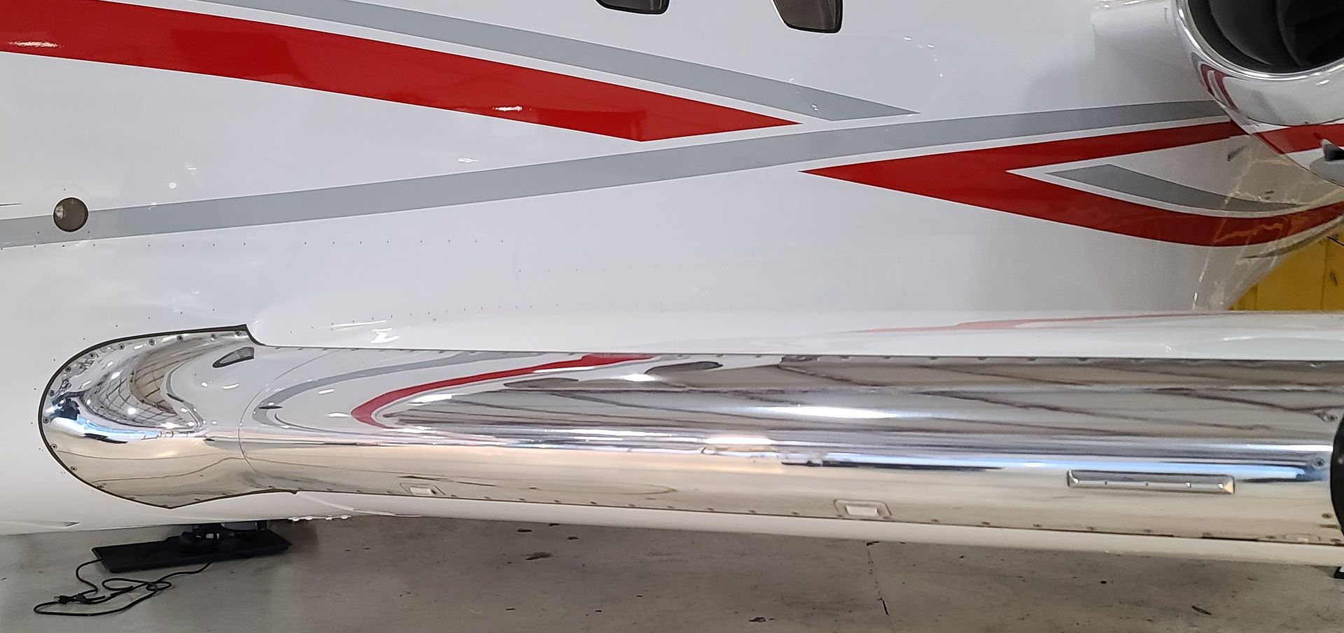 Close-up of a white and red jet airplane wing with a chrome wingtip, parked on a tarmac.