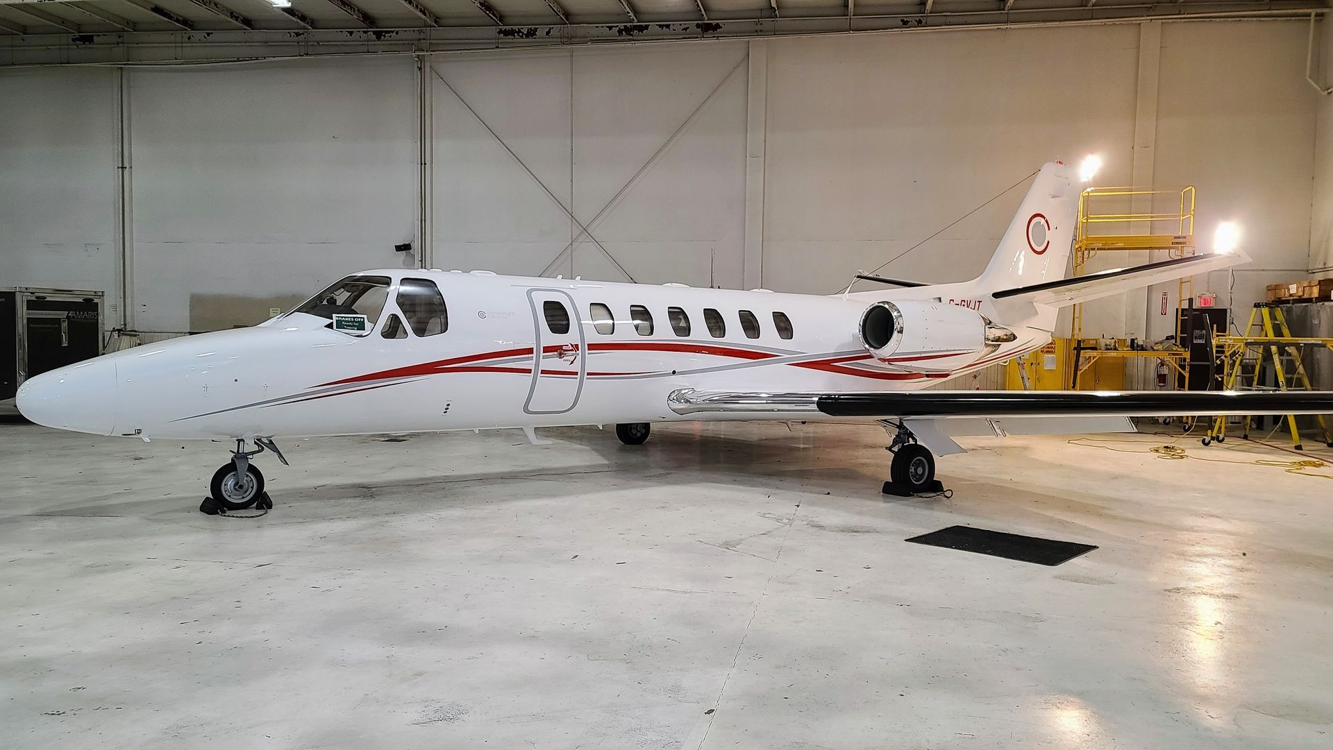 White private jet with red stripes parked inside a hangar.