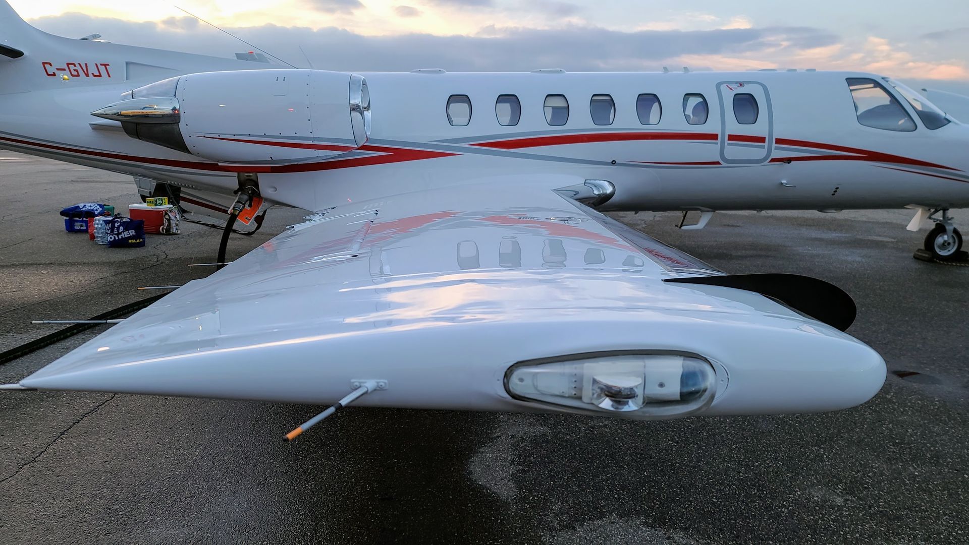 White and red private jet parked on a tarmac. Wing visible, with lights and detail.