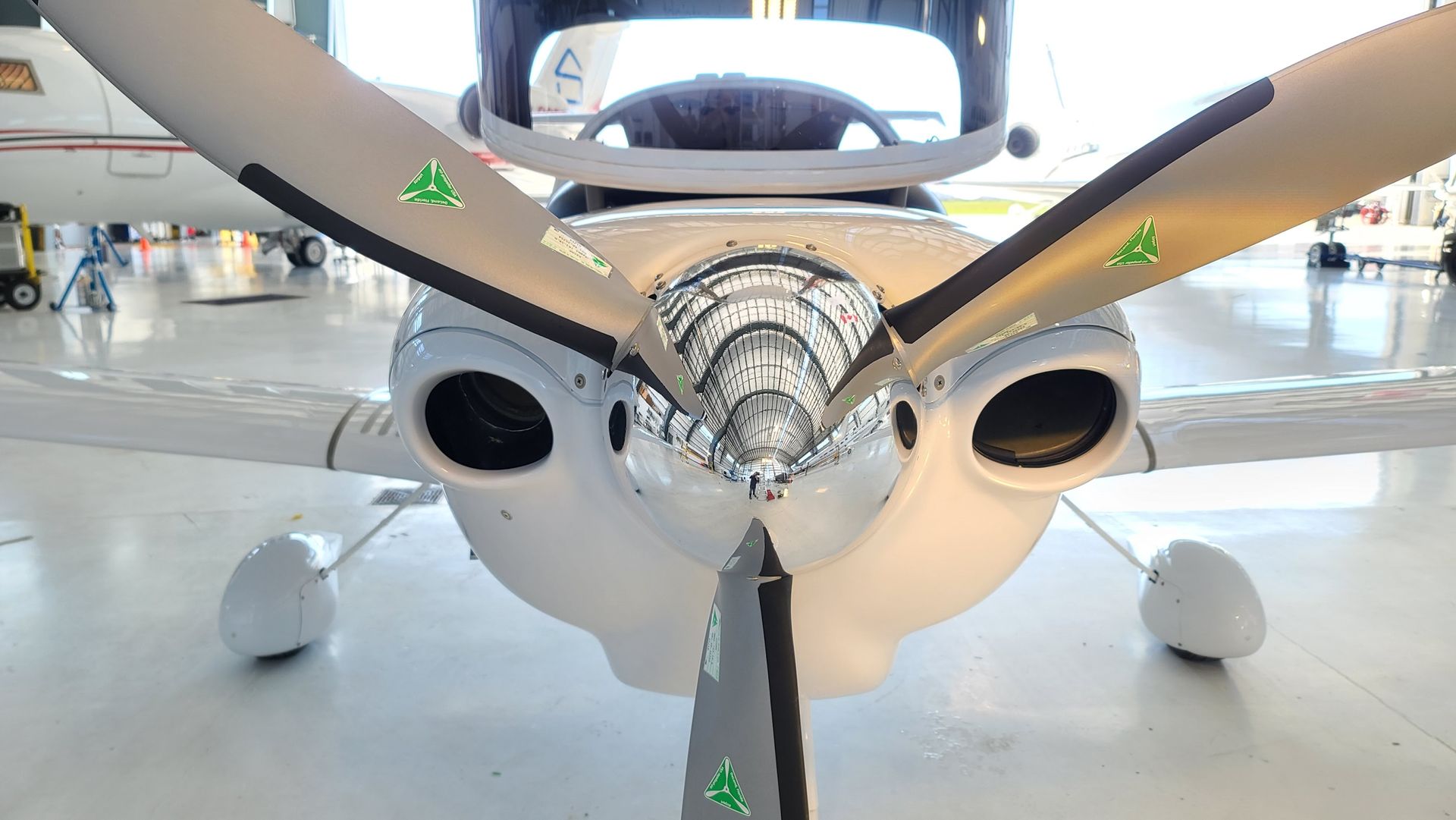 White airplane nose with propeller blades, in an airplane hangar.
