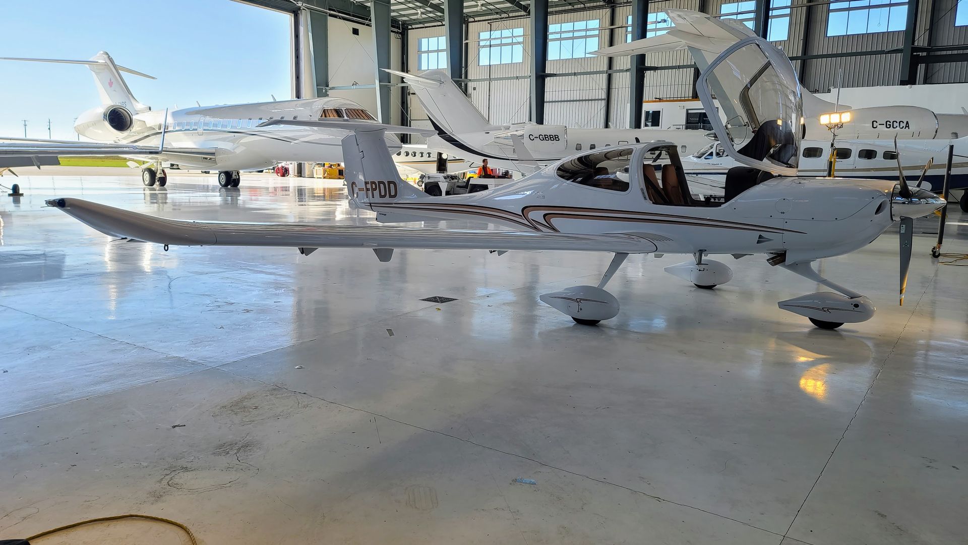 White airplane with open doors in a hangar, other aircraft in background.