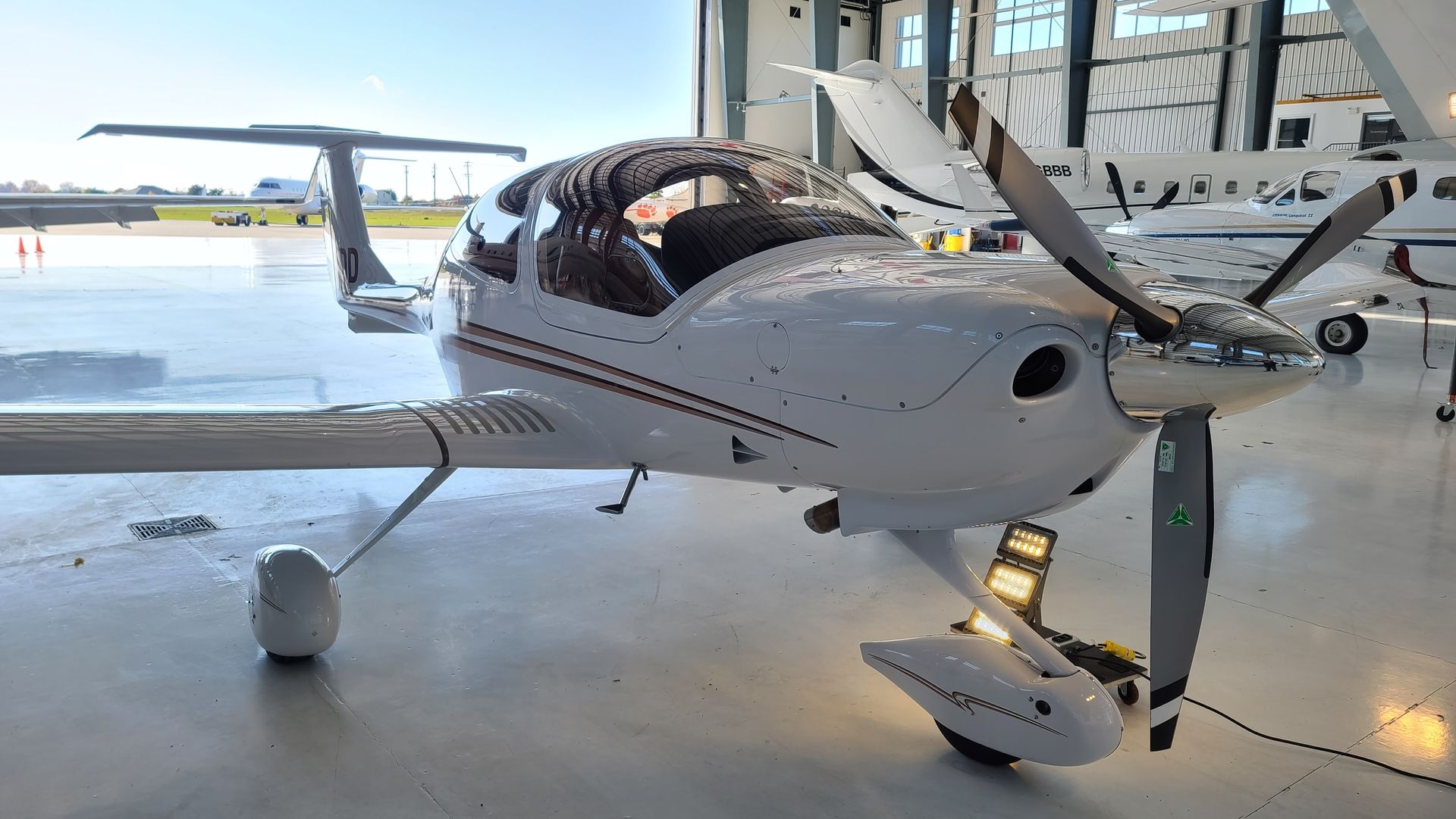 White and silver single-engine aircraft inside a hangar, with a propeller, nose gear, and wings.