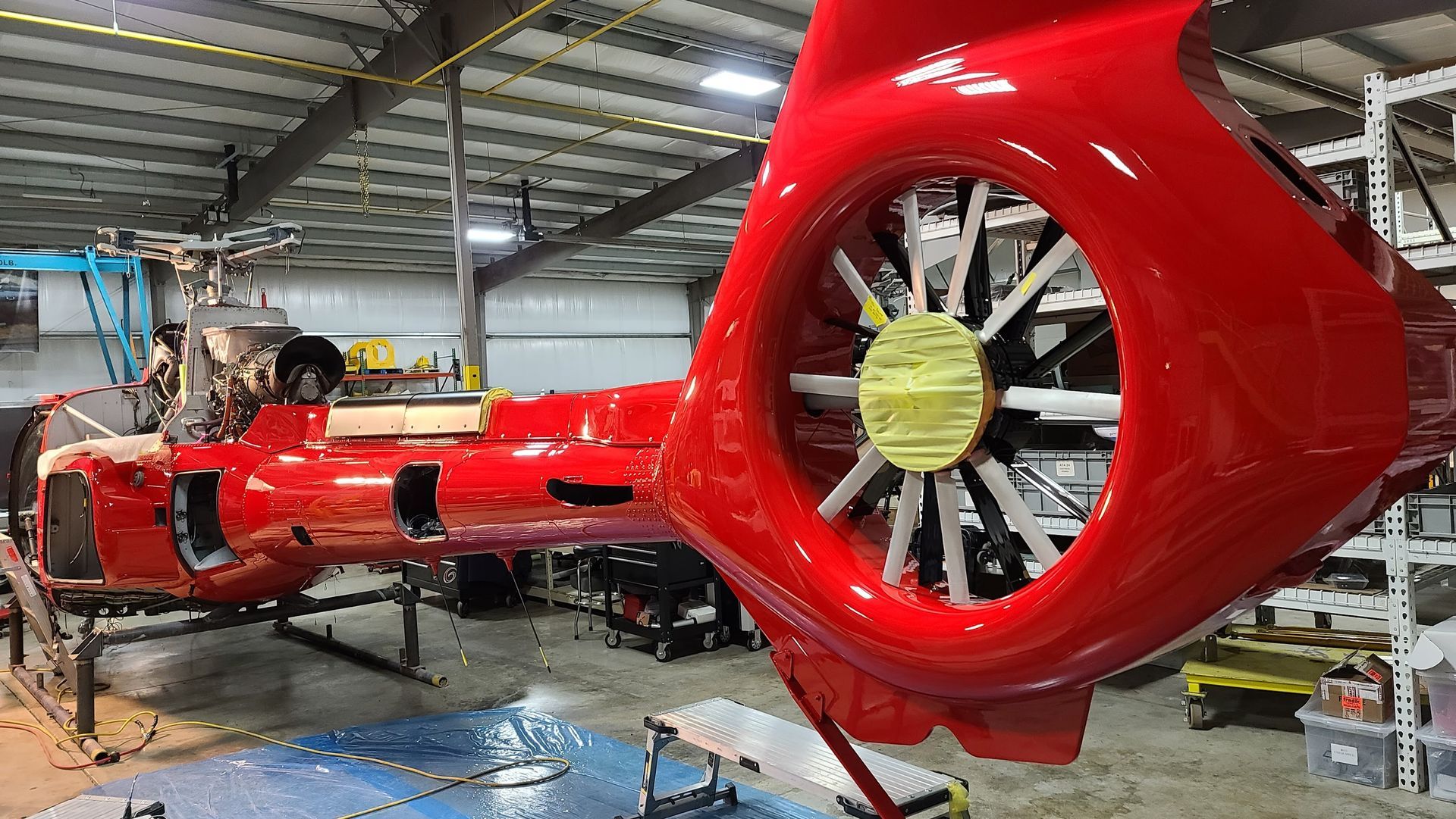 Red helicopter fuselage and tail rotor assembly in a hangar.