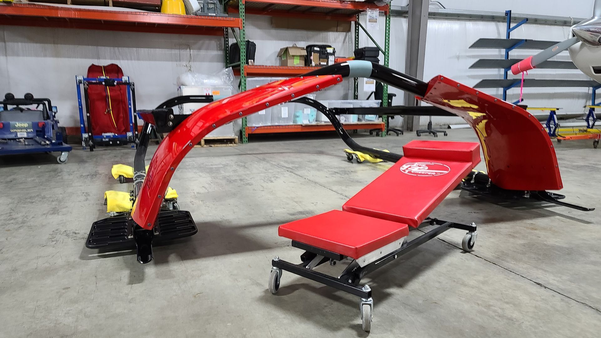 Red equipment, possibly for vehicle repair, with a bench and arched frame, in a workshop.