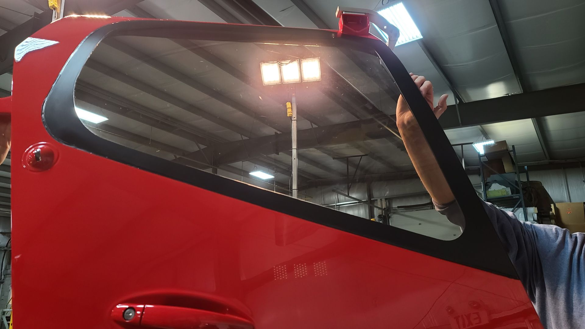 Red fire truck door with black trim; a person's arm reaches towards the window frame.