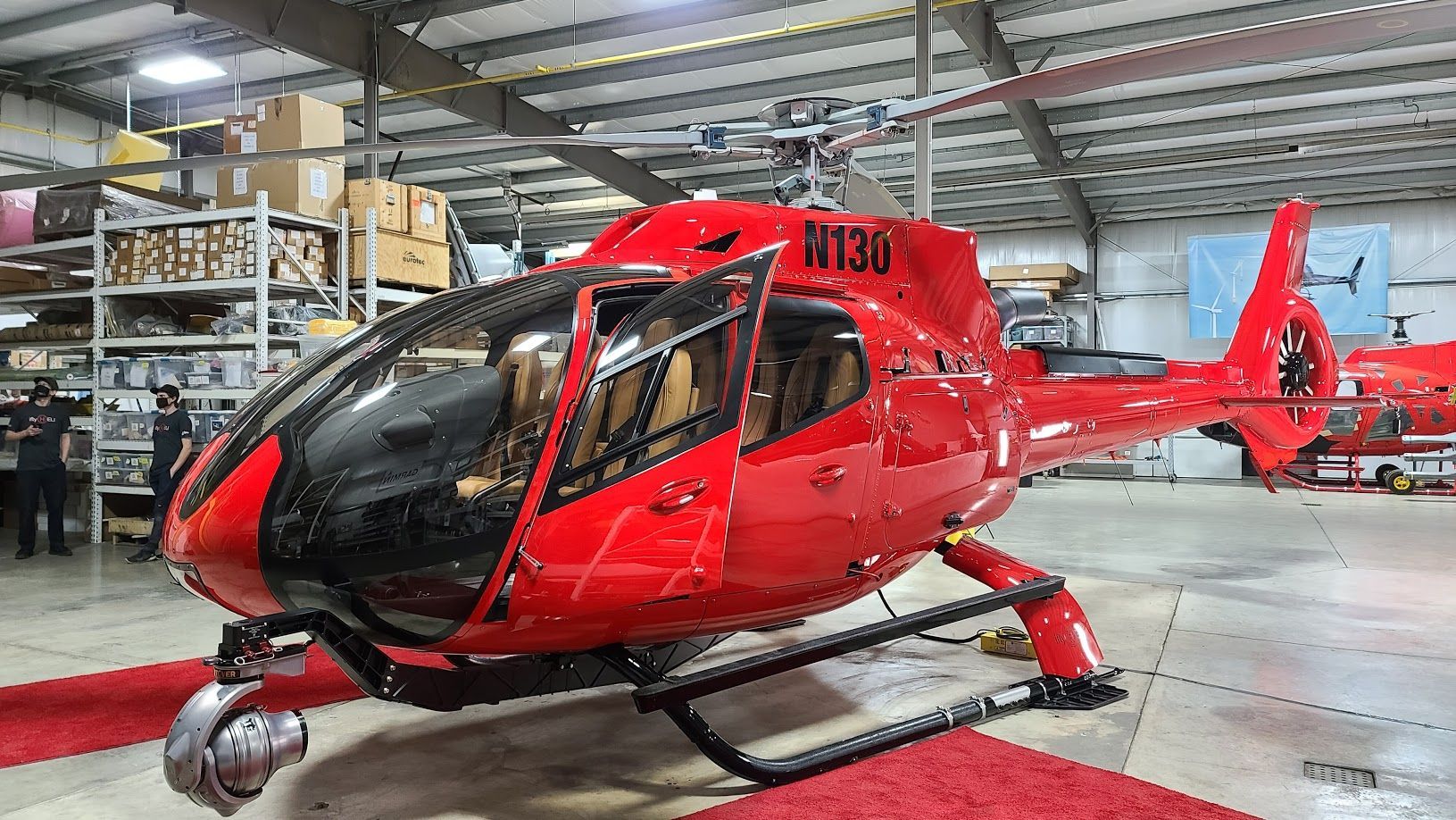 Red helicopter inside a hangar, doors open, on red carpet.