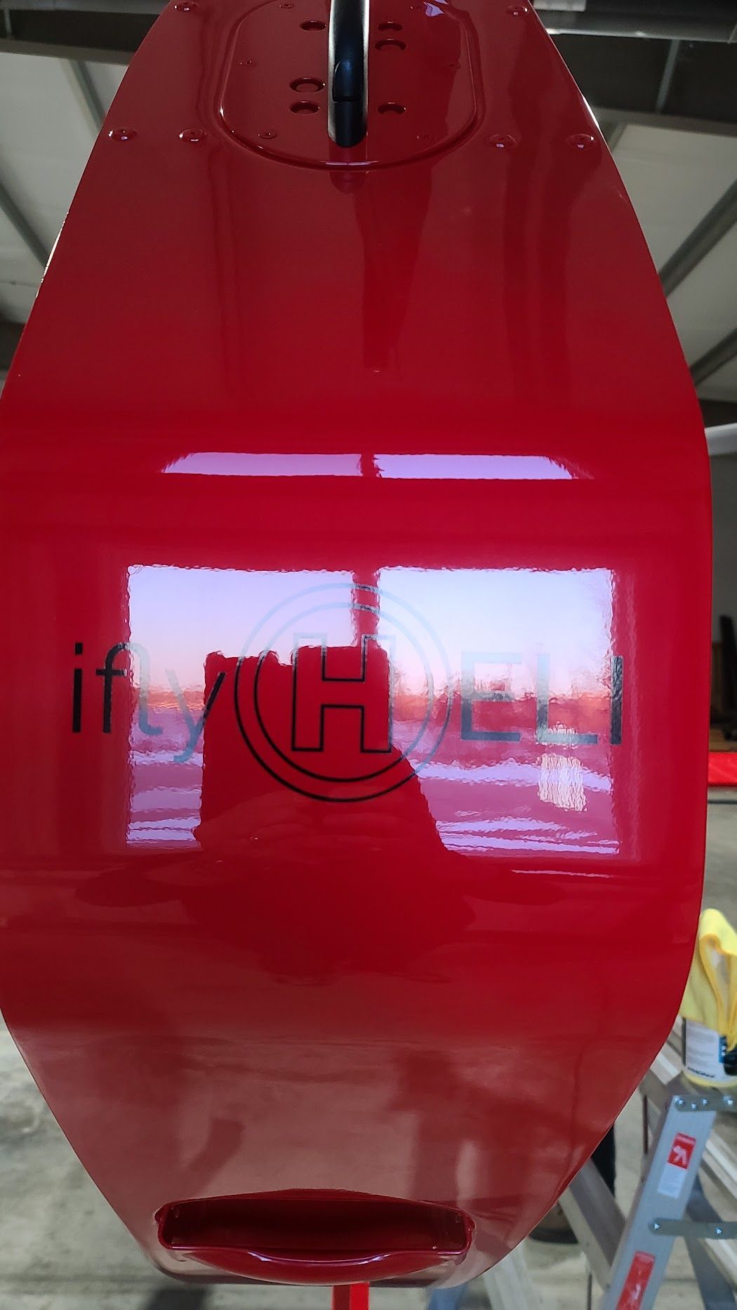 Red surfboard with glossy finish, reflecting a window with a logo.