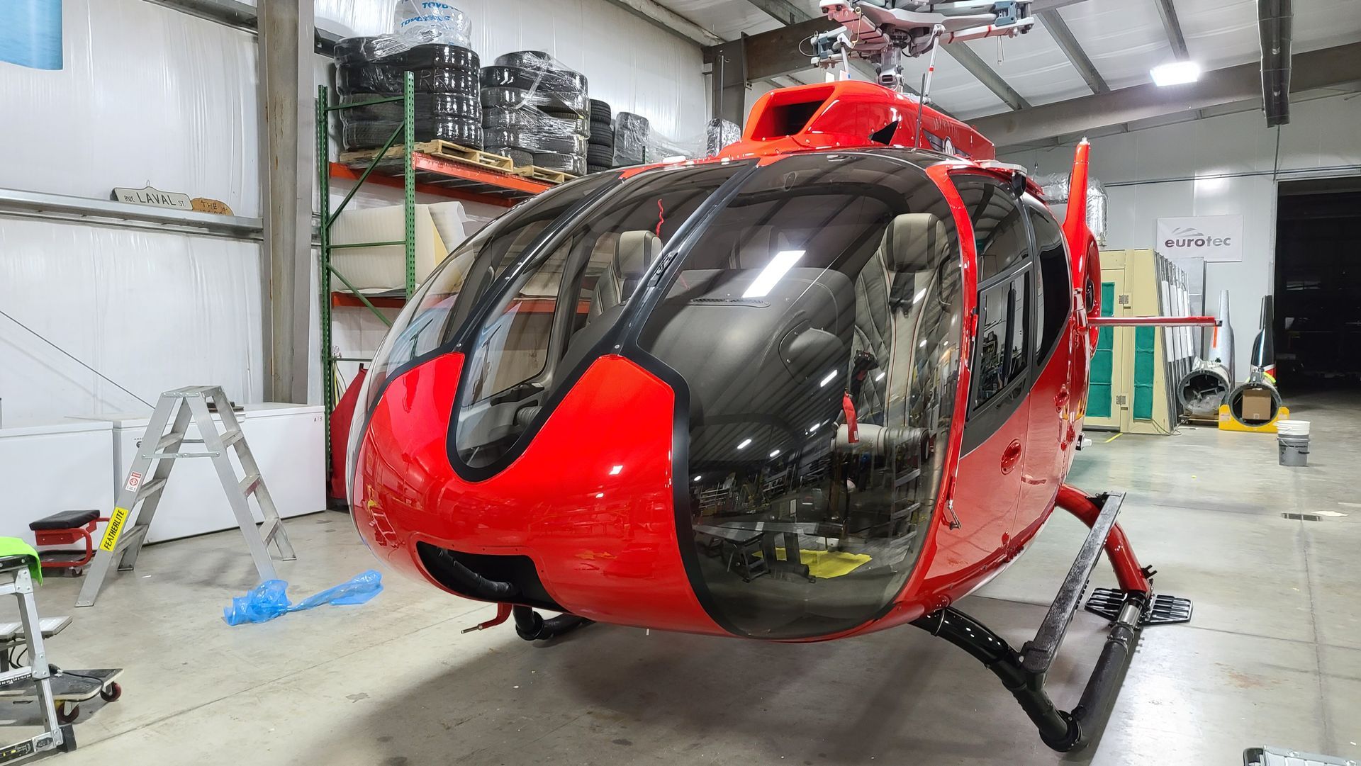 Red helicopter in a hangar, black struts, reflective windshield.
