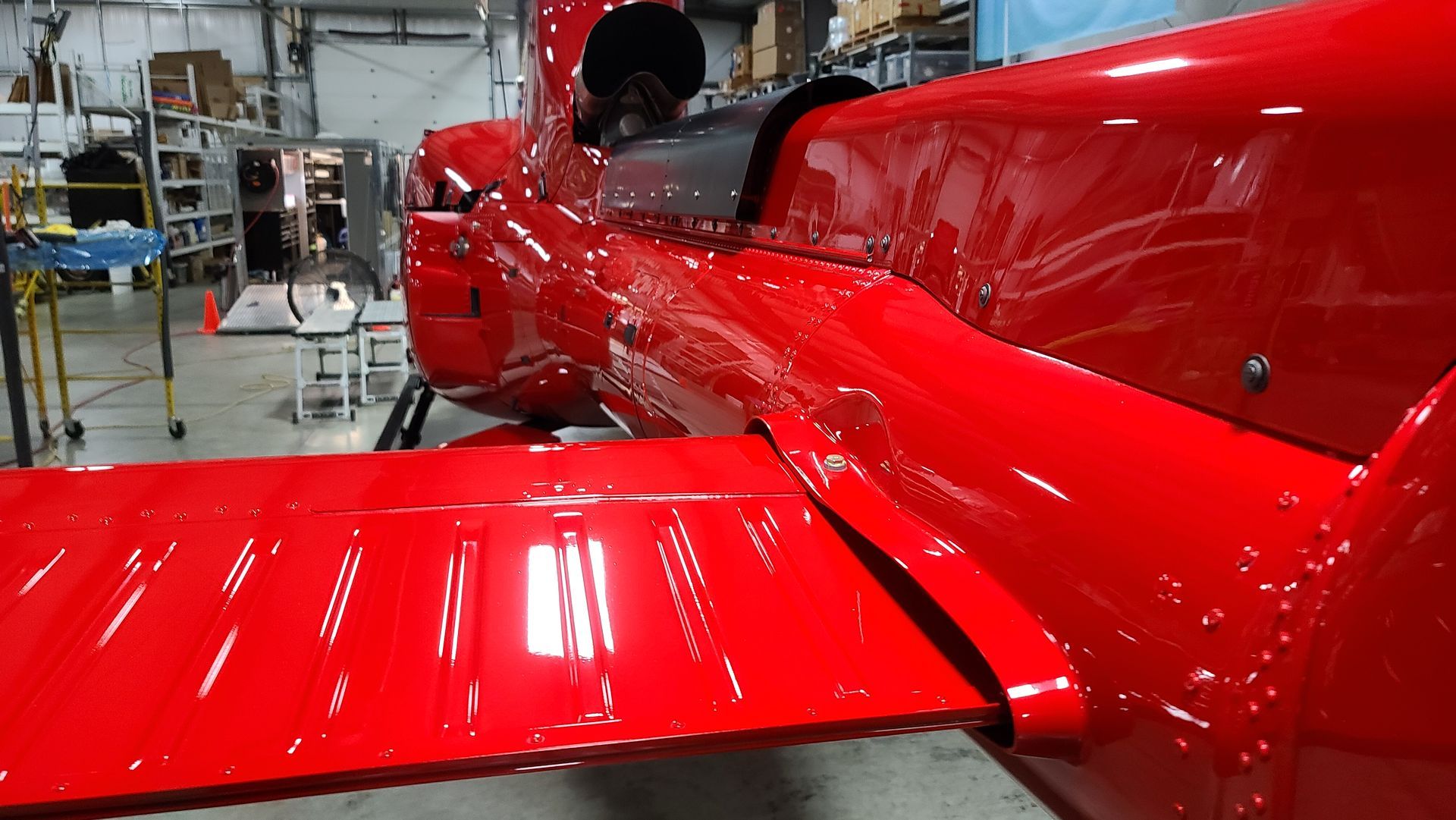 Red helicopter fuselage with wing in a workshop.