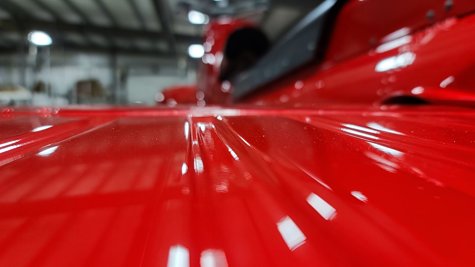 Close-up of a glossy, red truck bed. The ridges of the bed are visible, reflecting light.