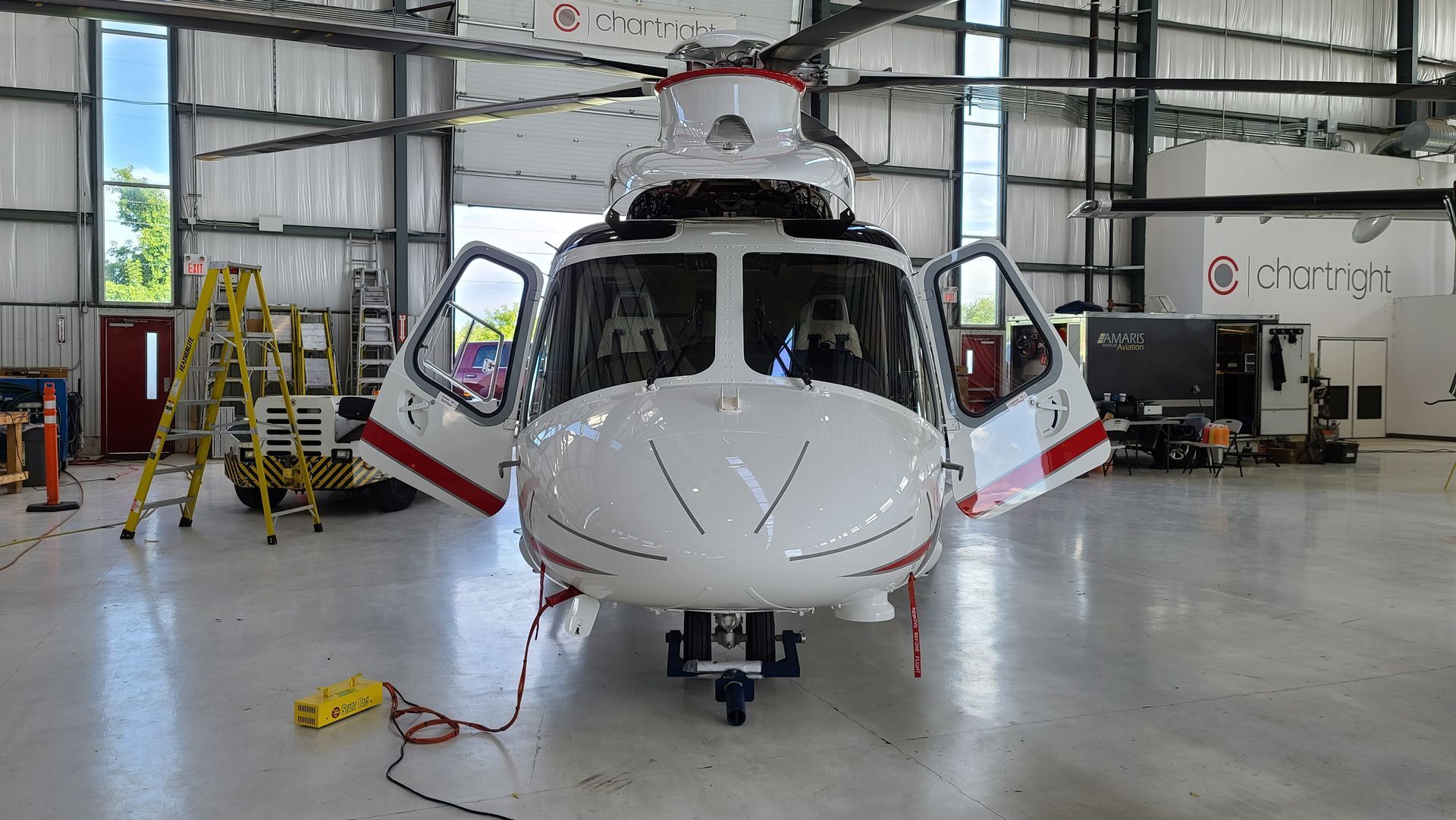 White helicopter with red stripes and open doors in a hangar.