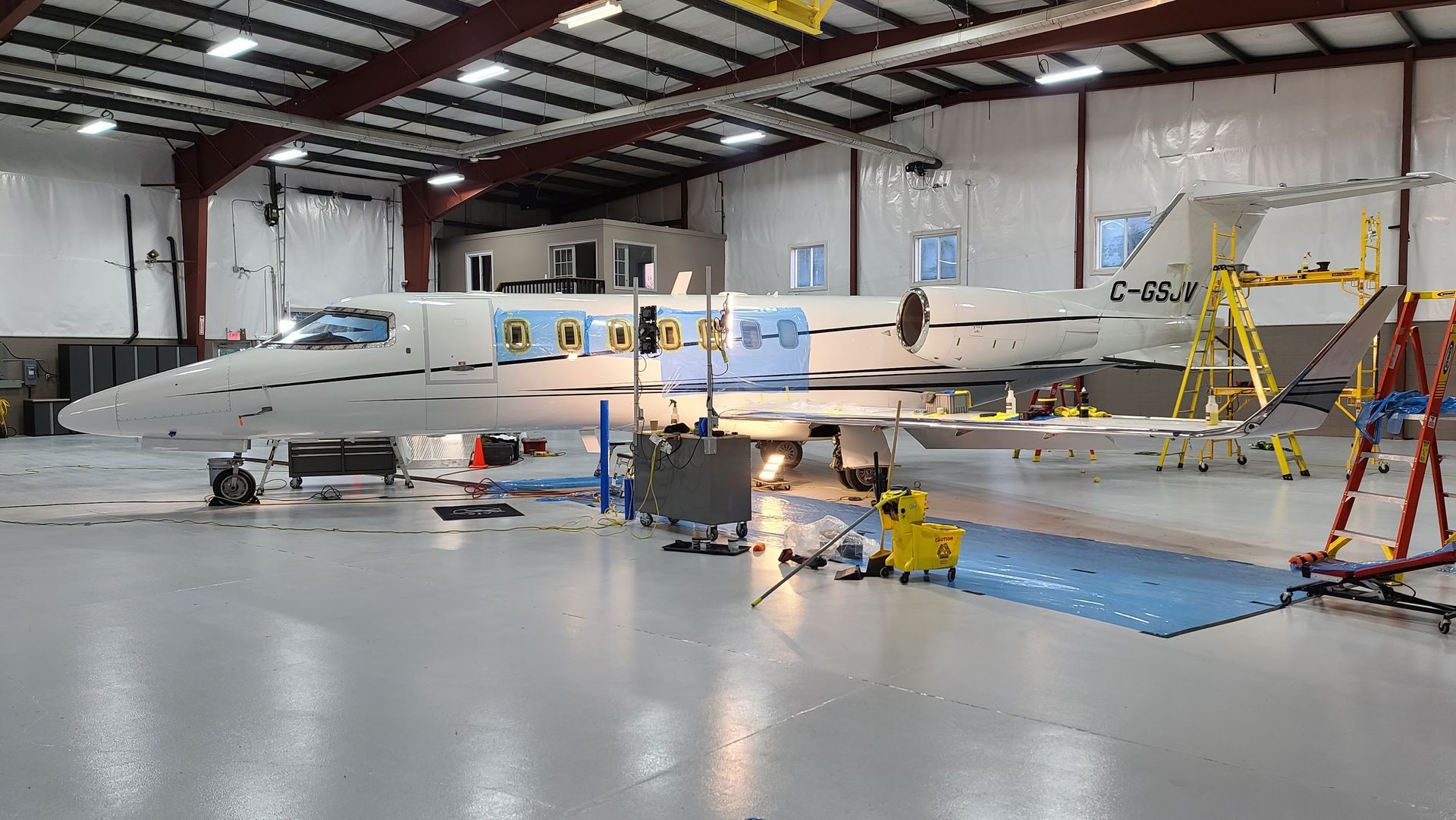 Airplane undergoing maintenance in a hangar. White fuselage, open panels, tools, and equipment are visible.