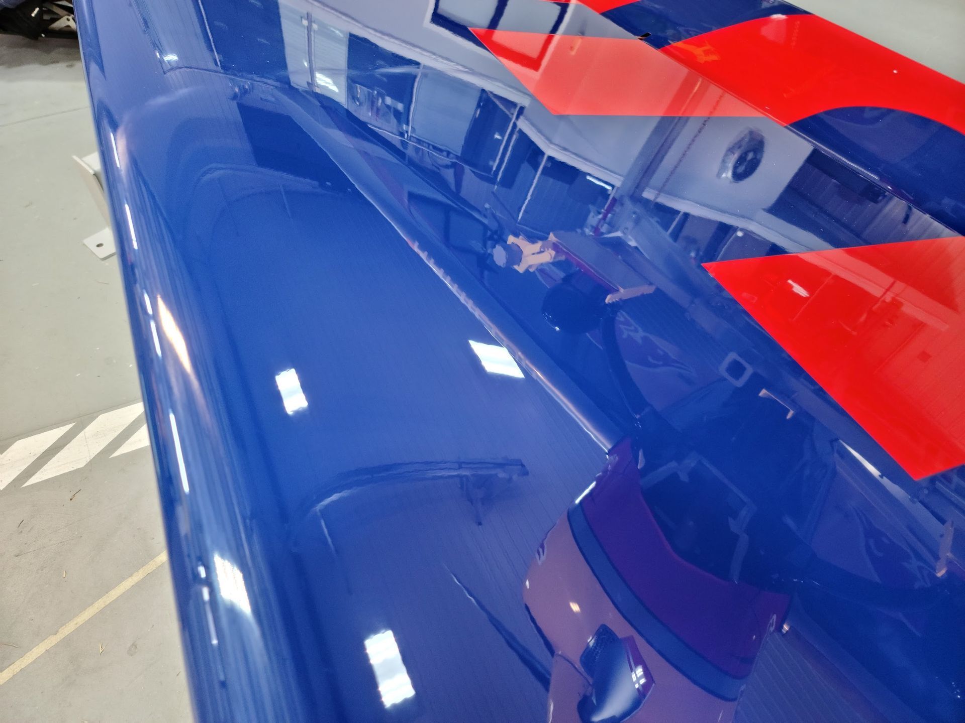 Blue and red painted vehicle roof reflecting a brightly lit indoor space.