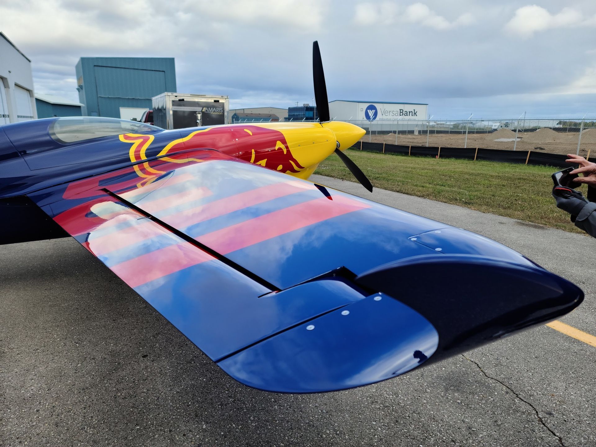 Red Bull acrobatic airplane wing, blue and red with yellow nose, parked on tarmac.