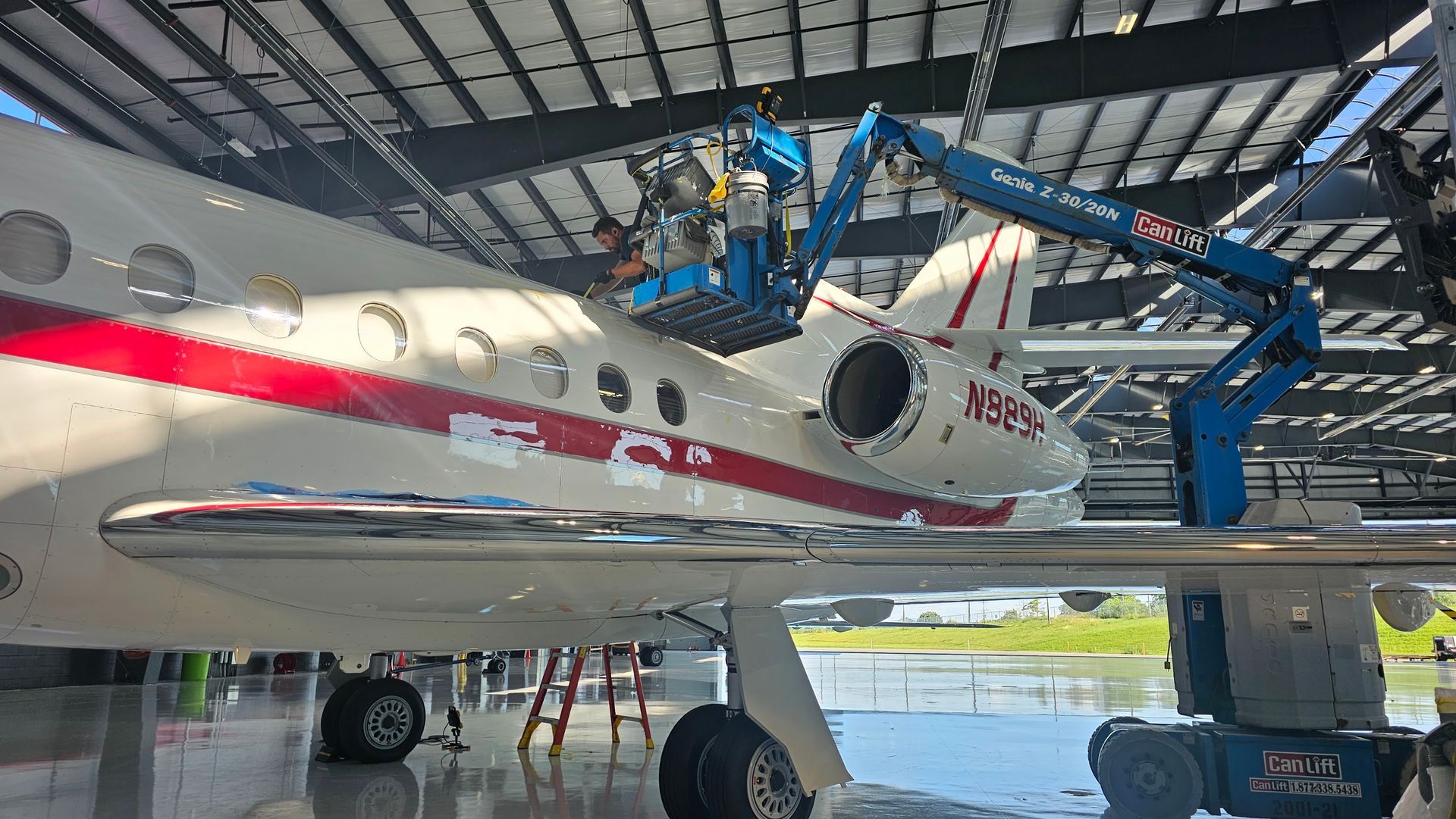 Aircraft being worked on inside a hangar, with a blue lift platform and a worker.